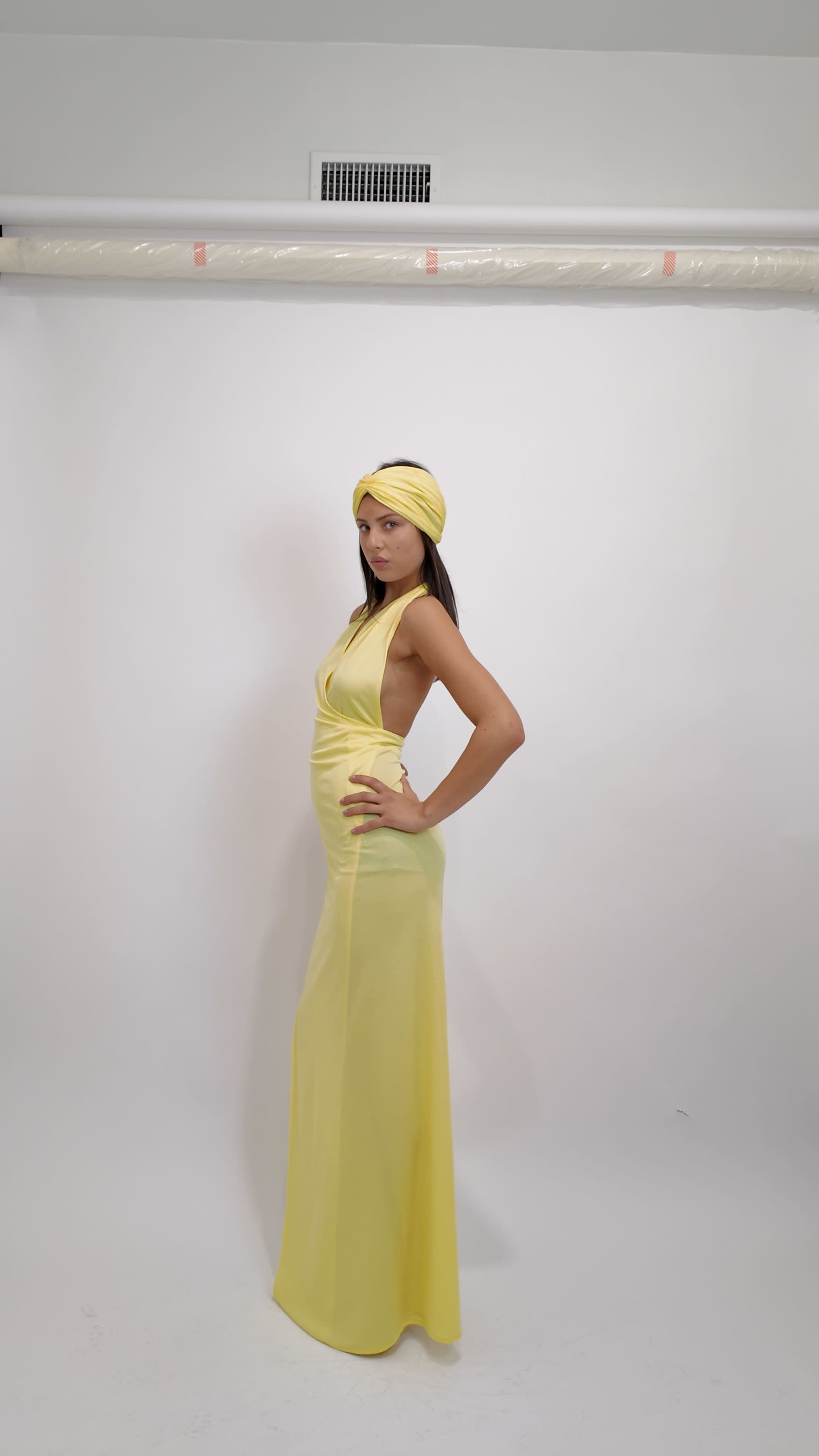 A model poses in a long yellow dress and matching headwrap against a plain white background.