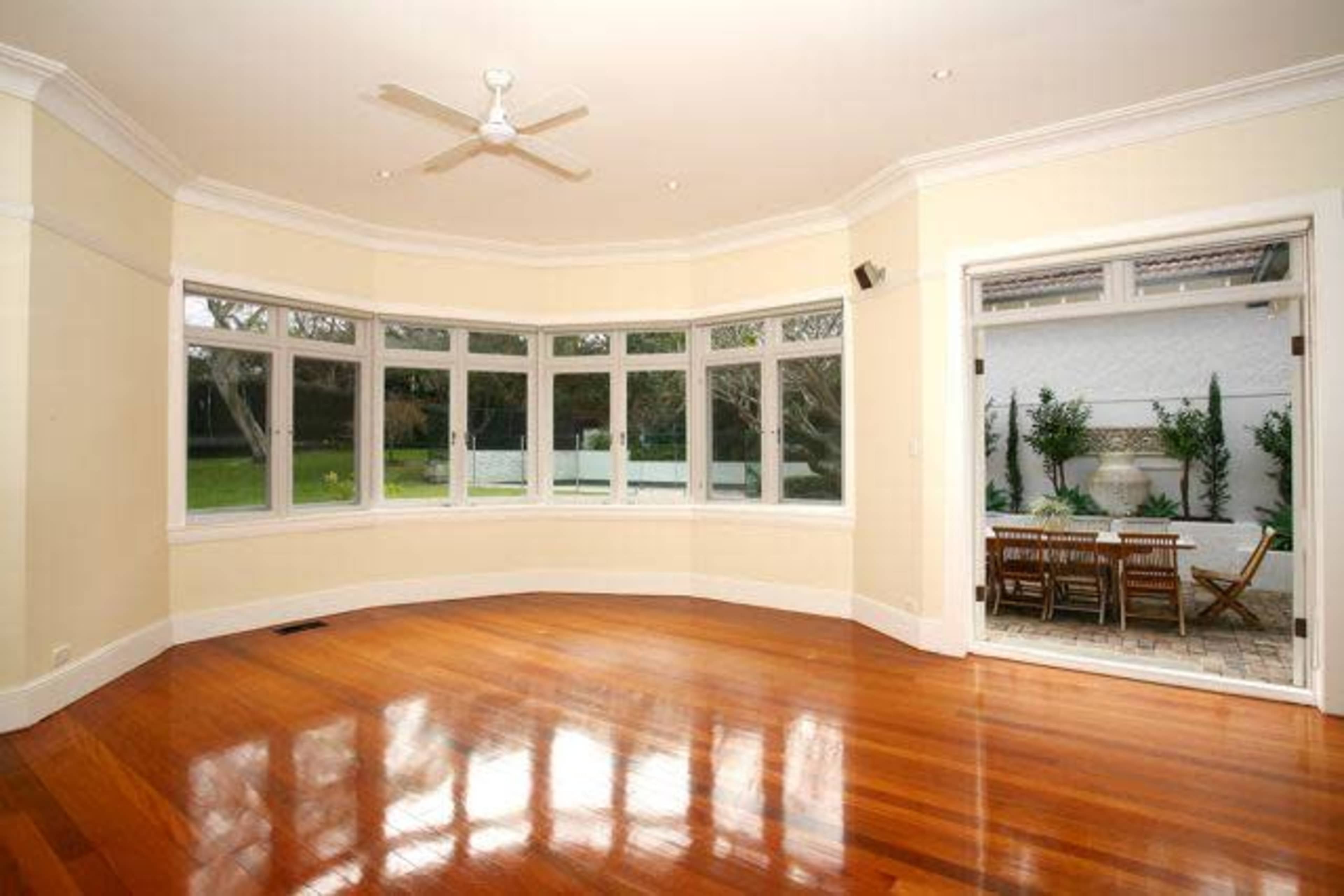 A spacious living room with large windows, wooden flooring, and a view of an outdoor patio area.