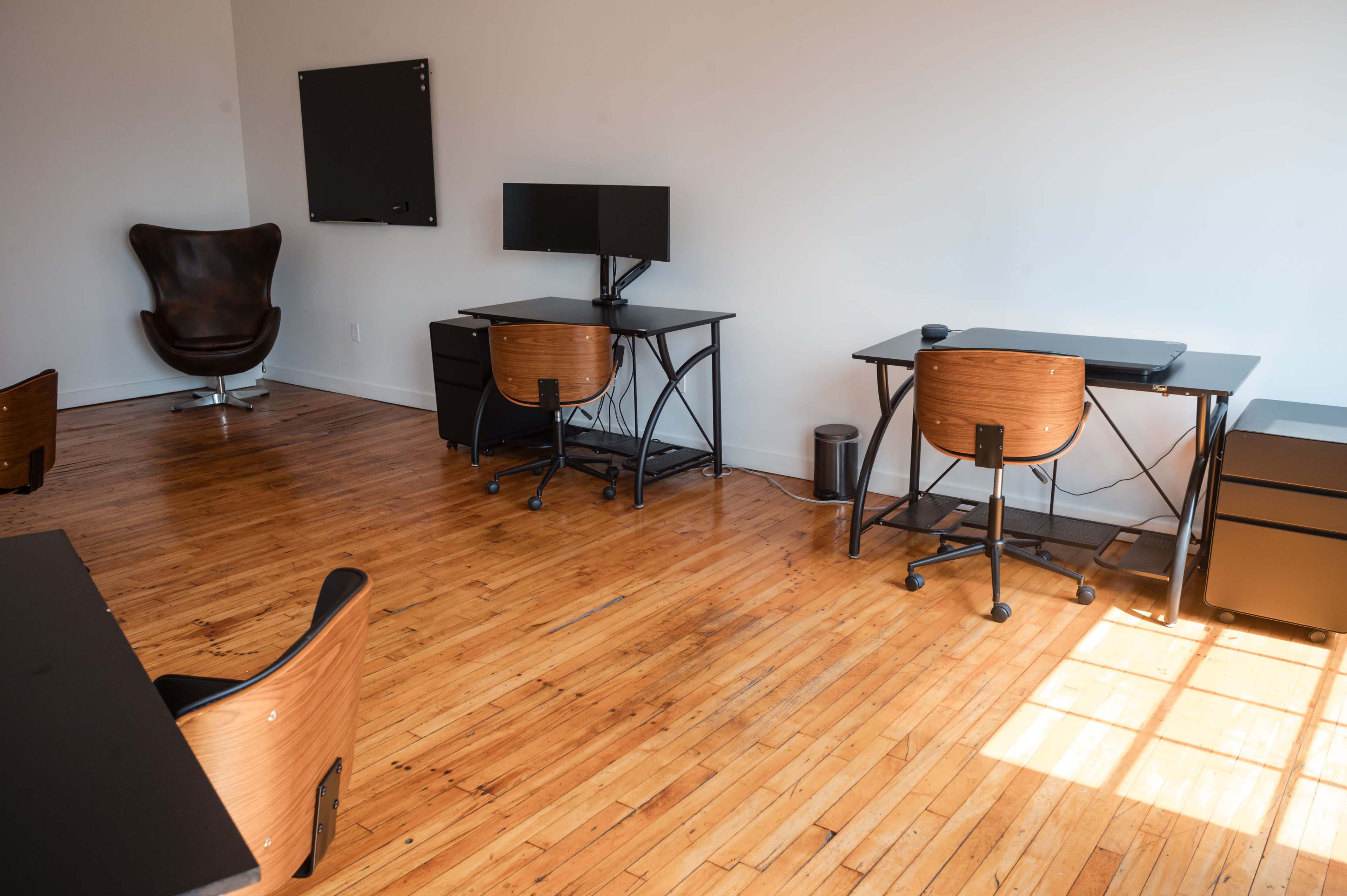 A spacious office with wooden flooring, featuring several desks, a computer monitor, and a large brown chair in the corner.