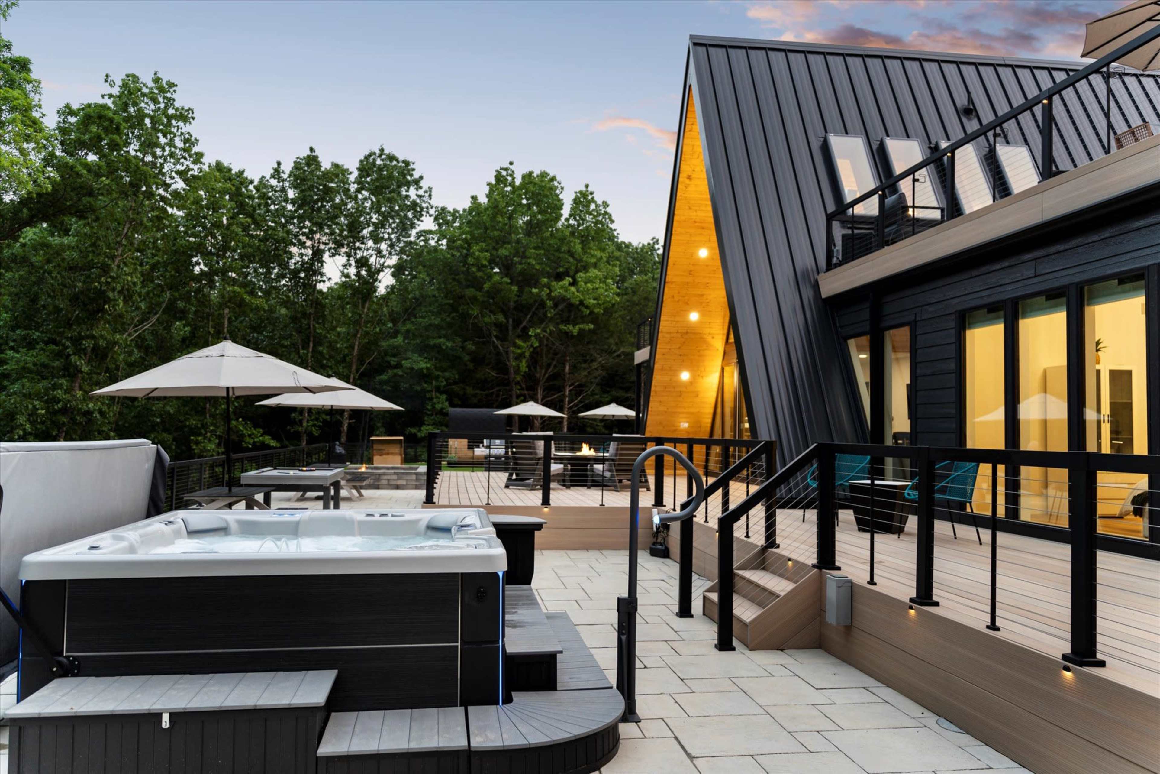 The image shows a modern outdoor space featuring a hot tub, wooden deck, and an angular building surrounded by trees.