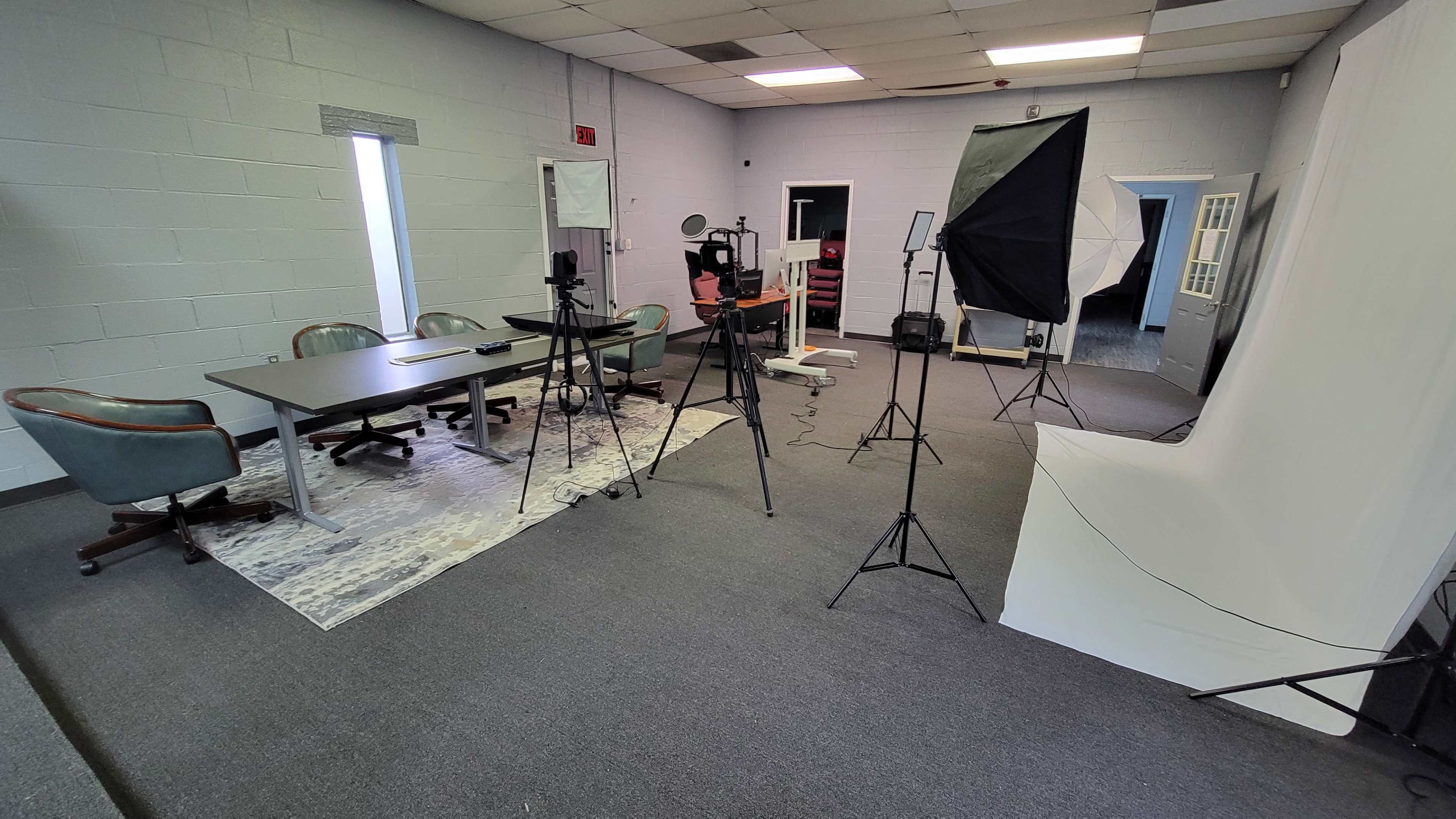 A professional studio space set up with a conference table, chairs, and lighting equipment for video production.