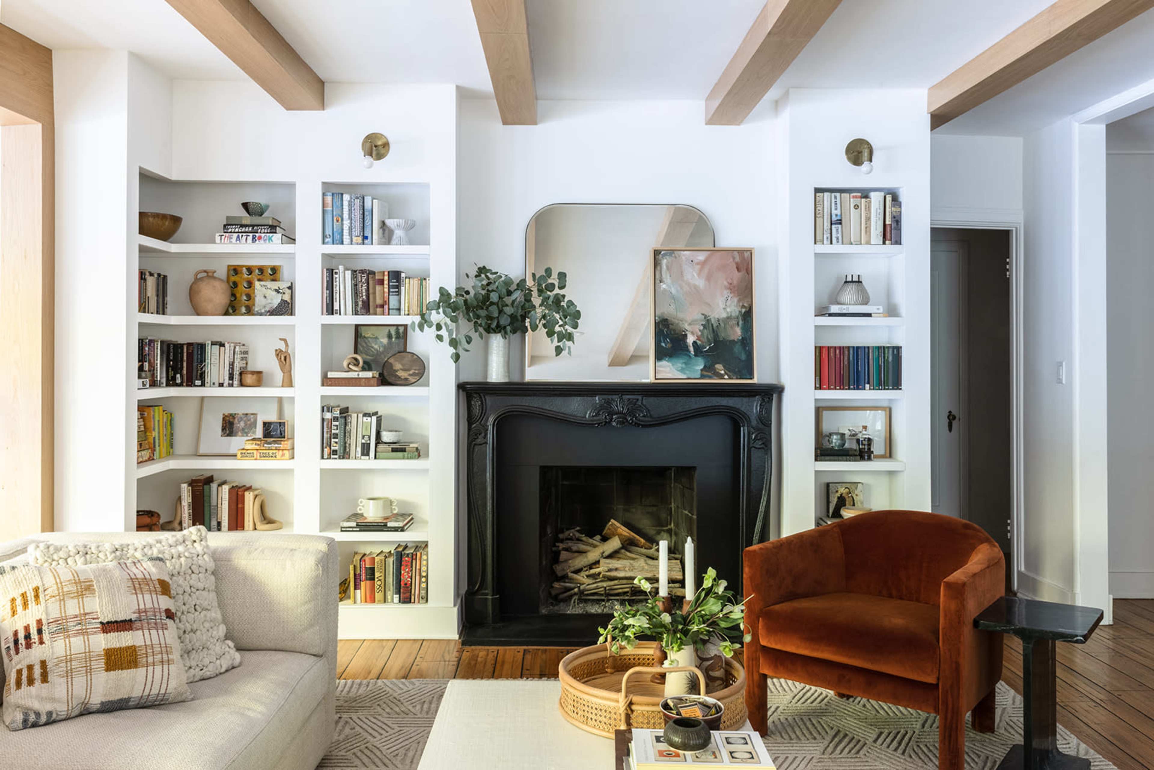 The living room features a black mantel fireplace surrounded by white bookshelves filled with books and decorative items, with a comfortable sofa and an orange chair.