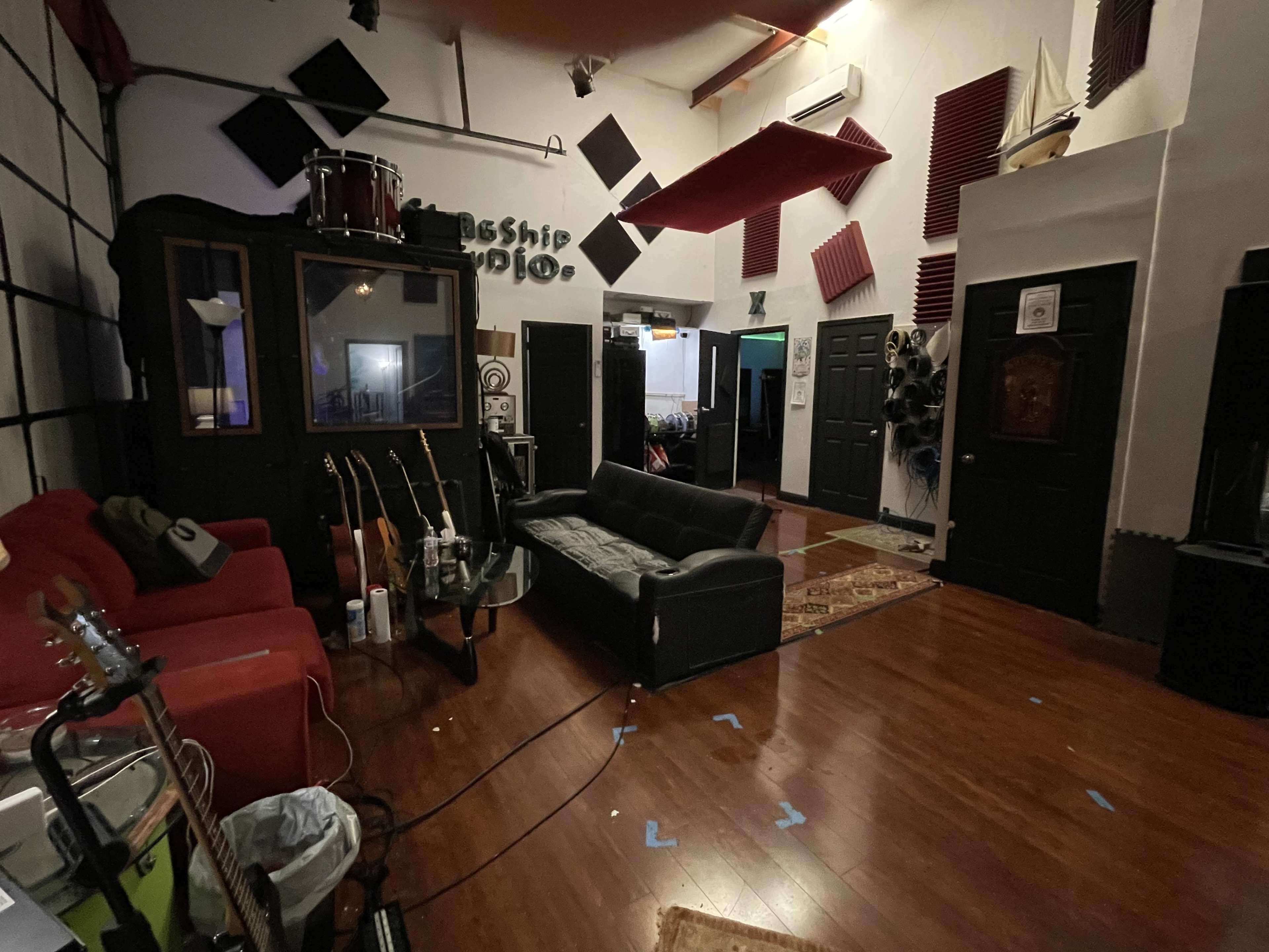 A recording studio with a black couch, a red sofa, guitars on stands, and soundproofing panels on the walls.
