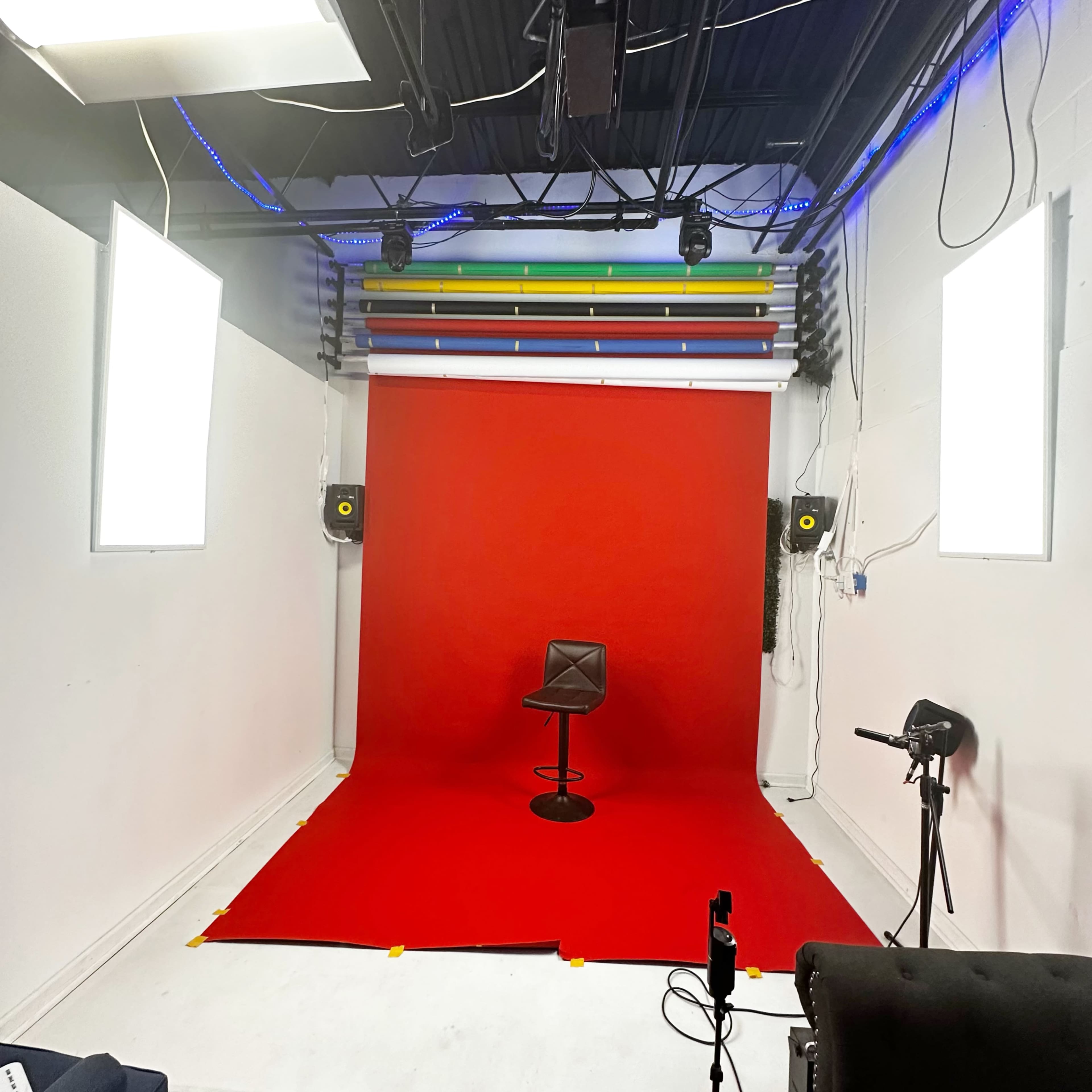 A small studio space with a red backdrop, a single black stool, and studio lighting on either side.