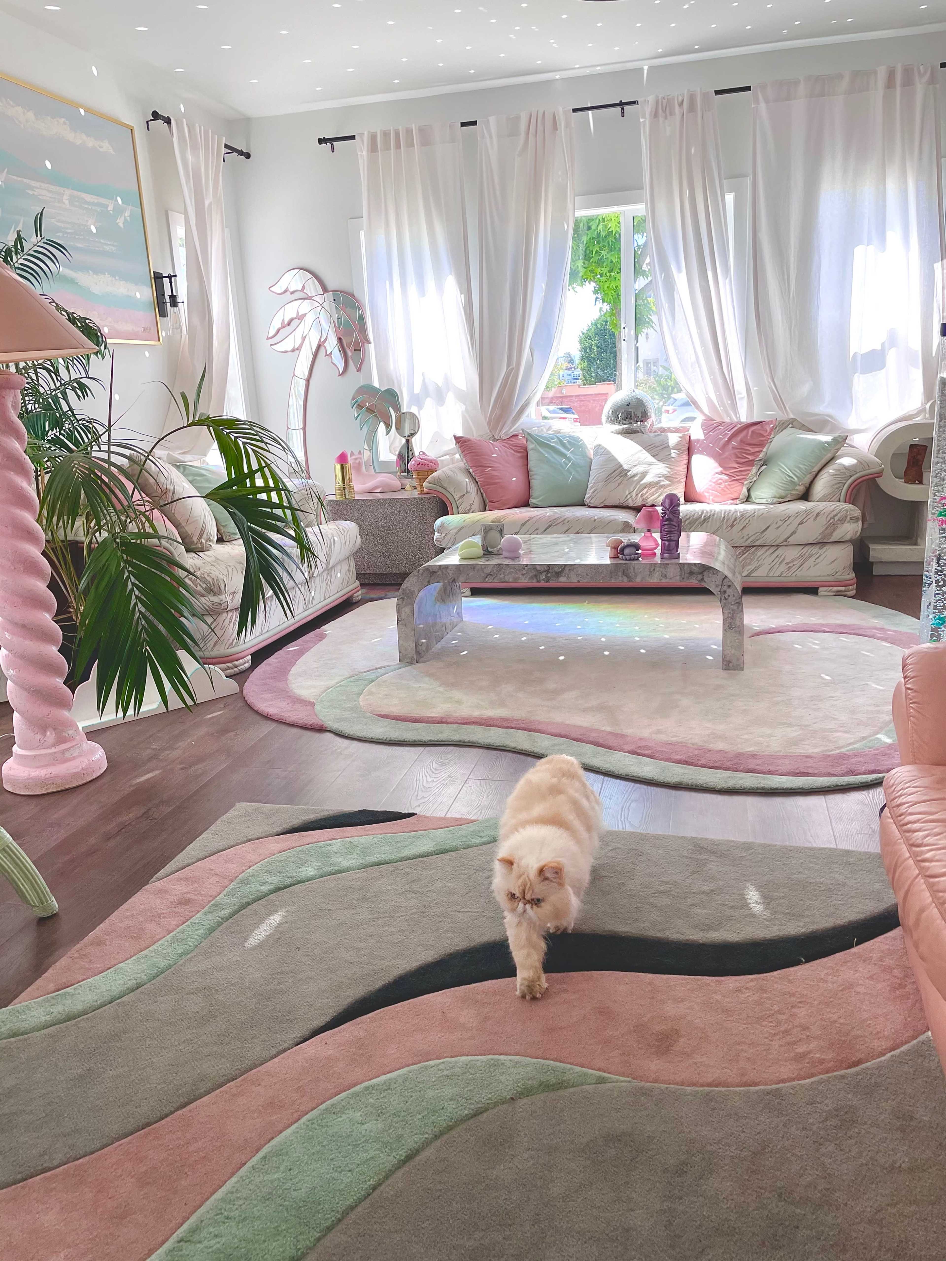 A light-filled living room features plush sofas, a modern coffee table, and a cat walking across a patterned rug.