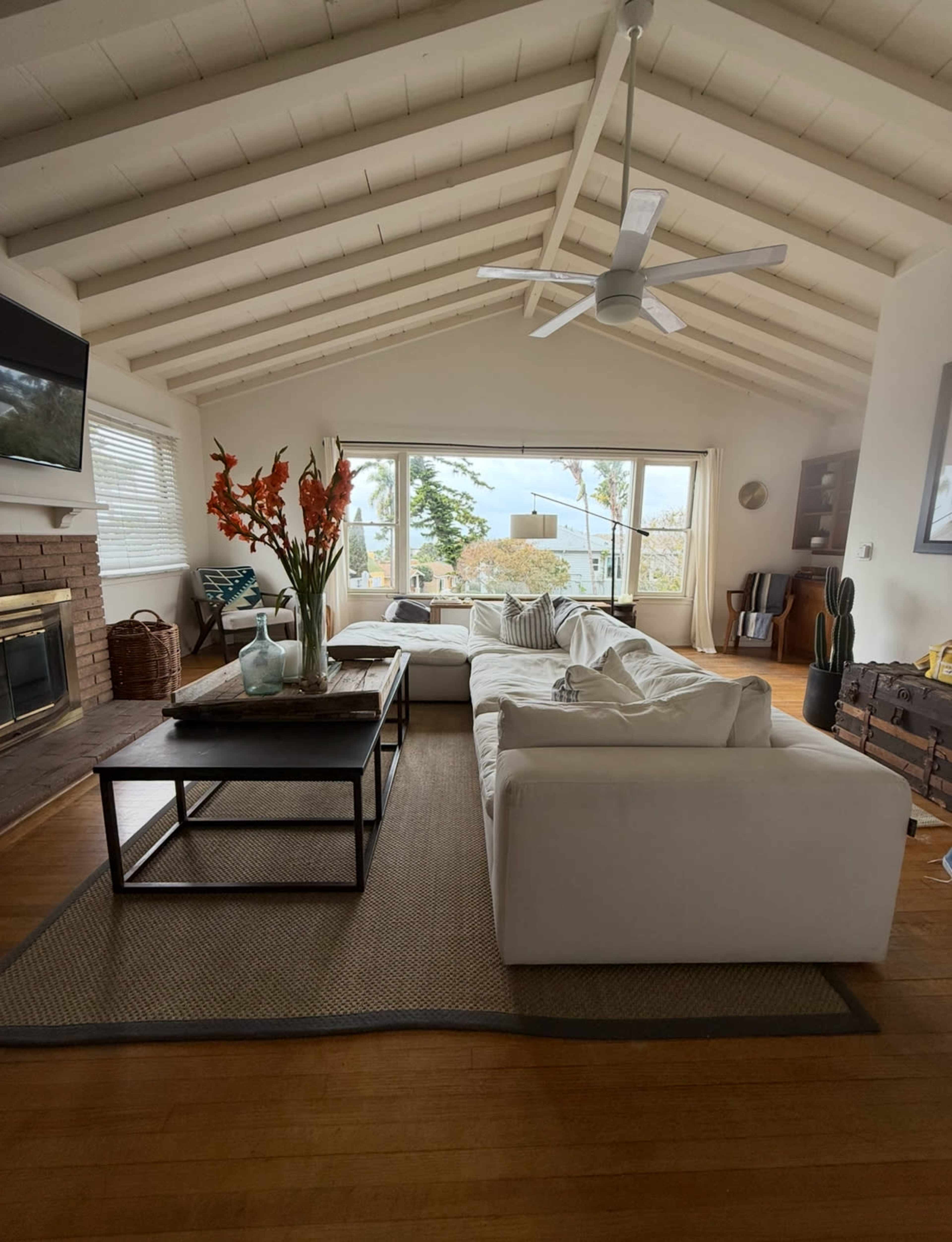 The living room features a white sectional sofa, a black coffee table, and large windows showcasing a scenic view outside.