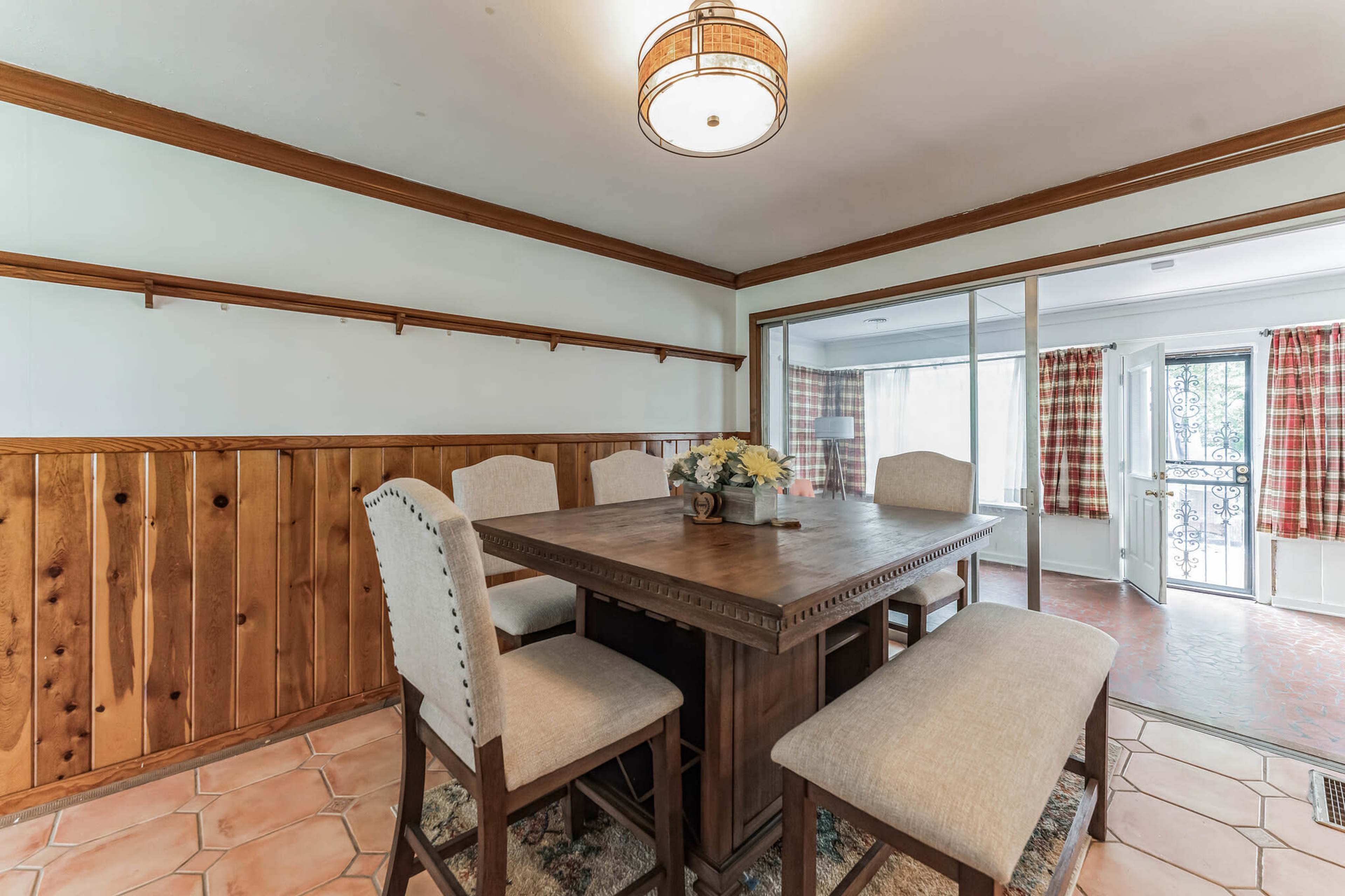 A dining room features a wooden table surrounded by upholstered chairs, with a window looking out to a patio.
