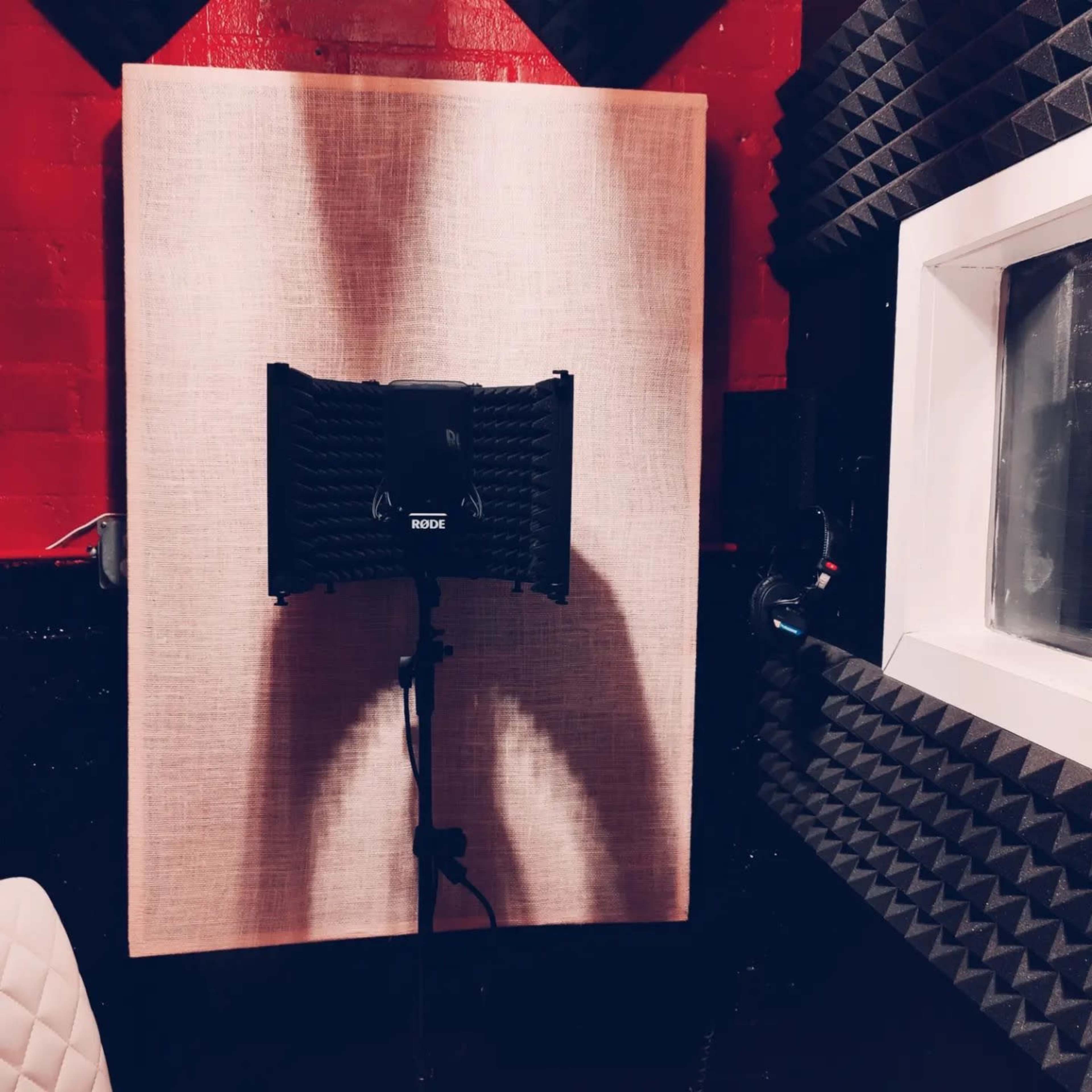 The image shows a soundproof recording studio with acoustic panels on the walls and a microphone positioned behind a pop filter.