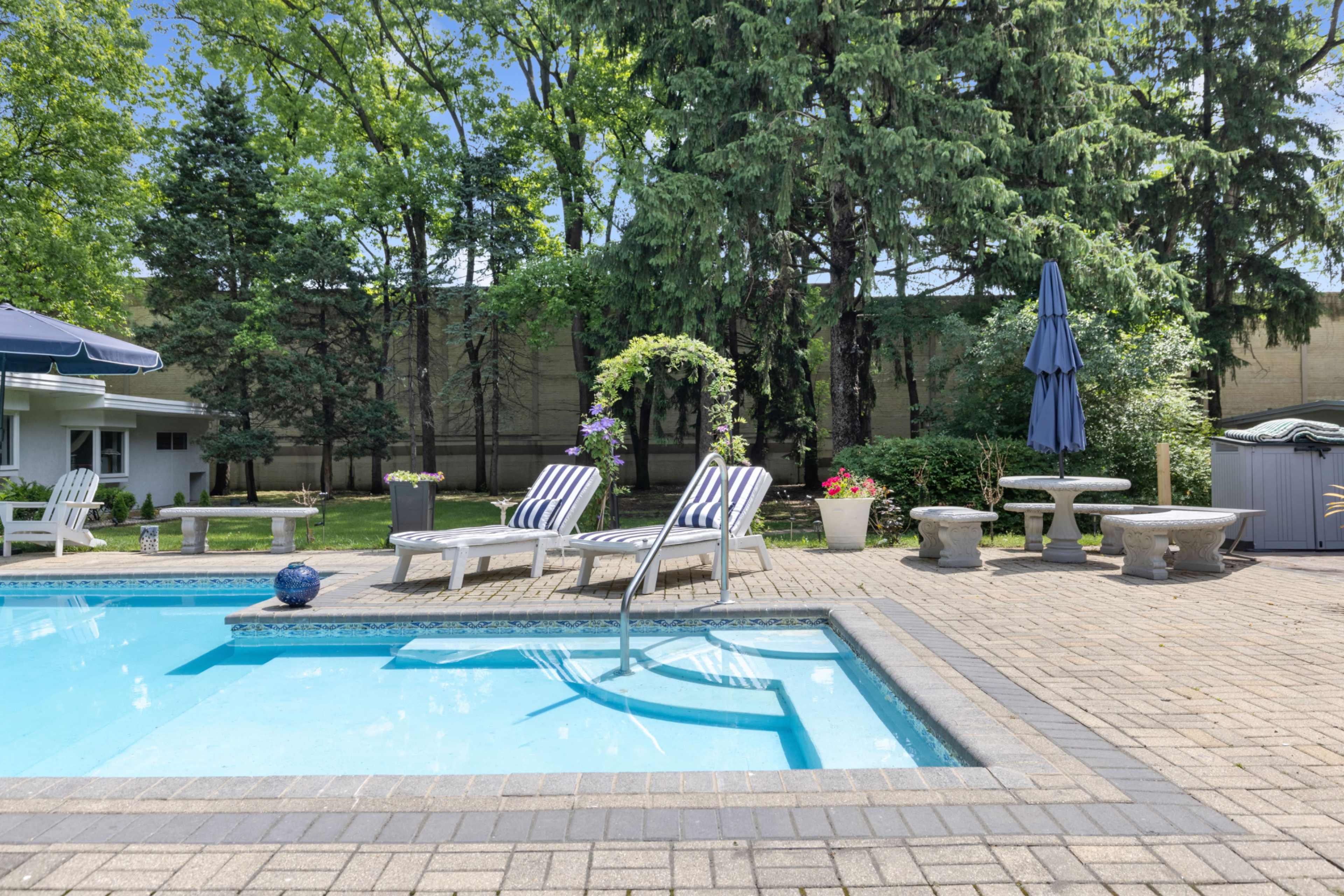 A backyard features a swimming pool with lounge chairs, surrounded by trees and landscaped areas.