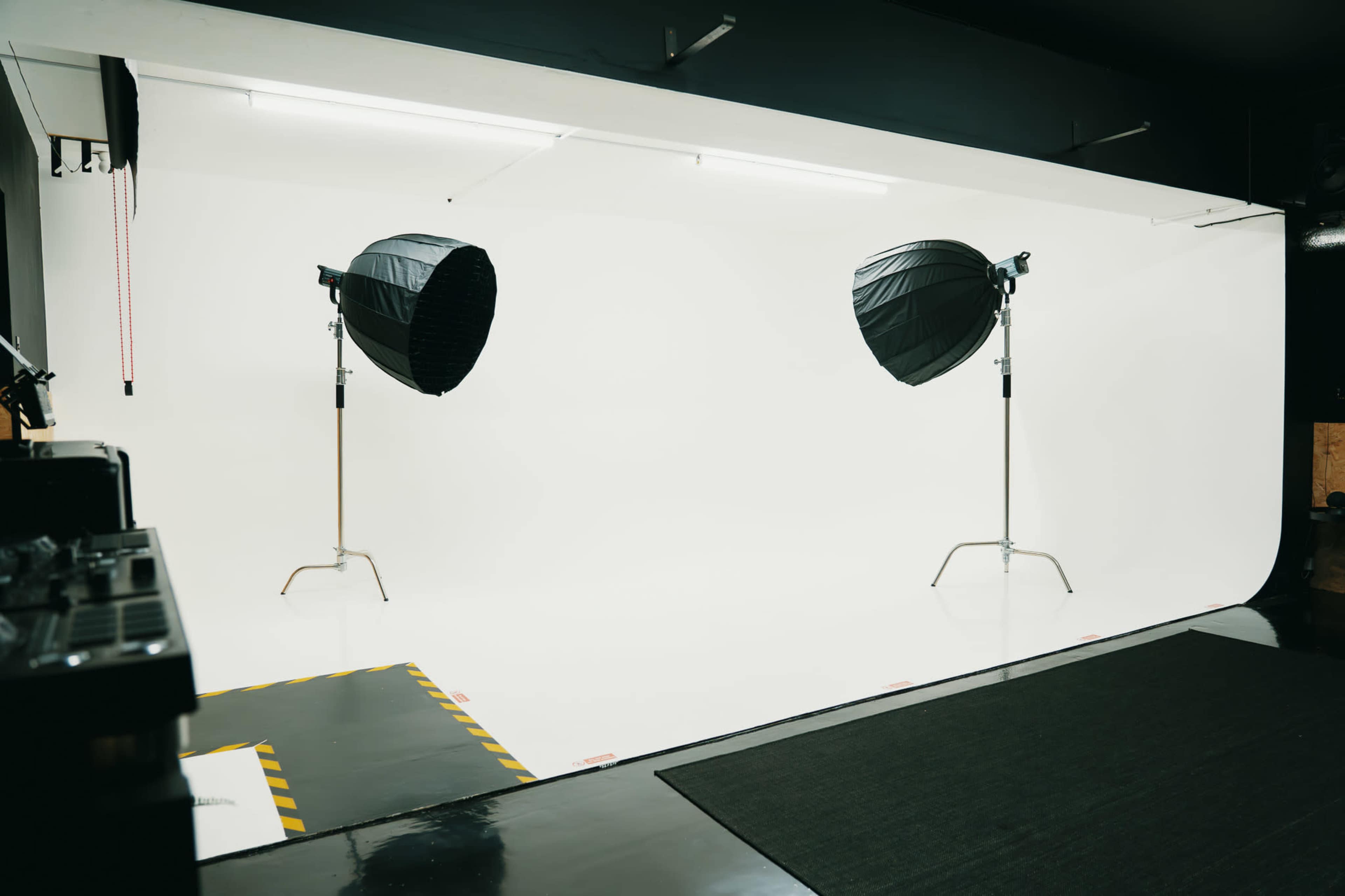 The image shows a photography studio with two large softbox lights positioned on stands, illuminating a seamless white backdrop.
