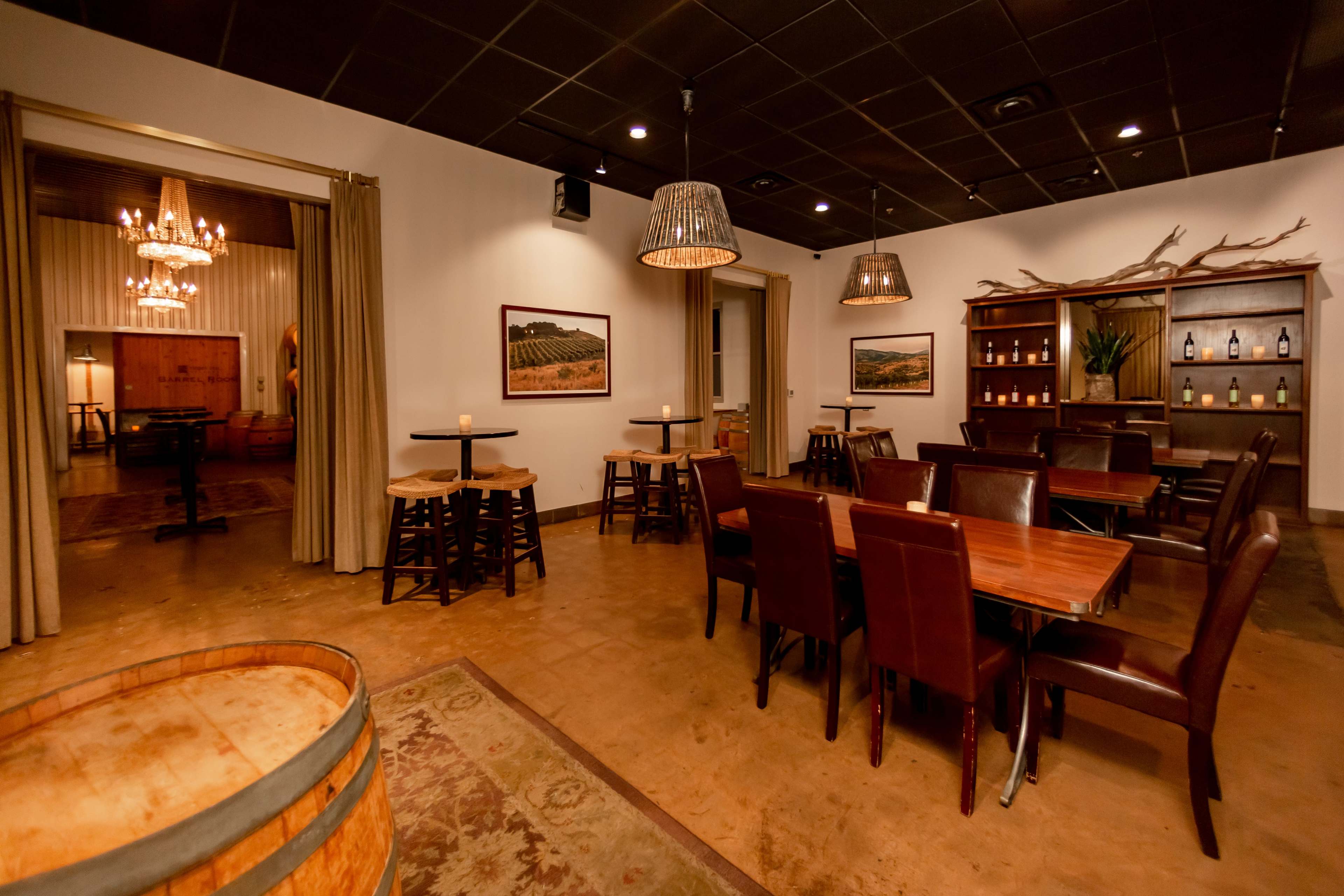 A dining area with wooden tables, leather chairs, decorative lighting fixtures, and a bar area lined with shelves displaying bottles.