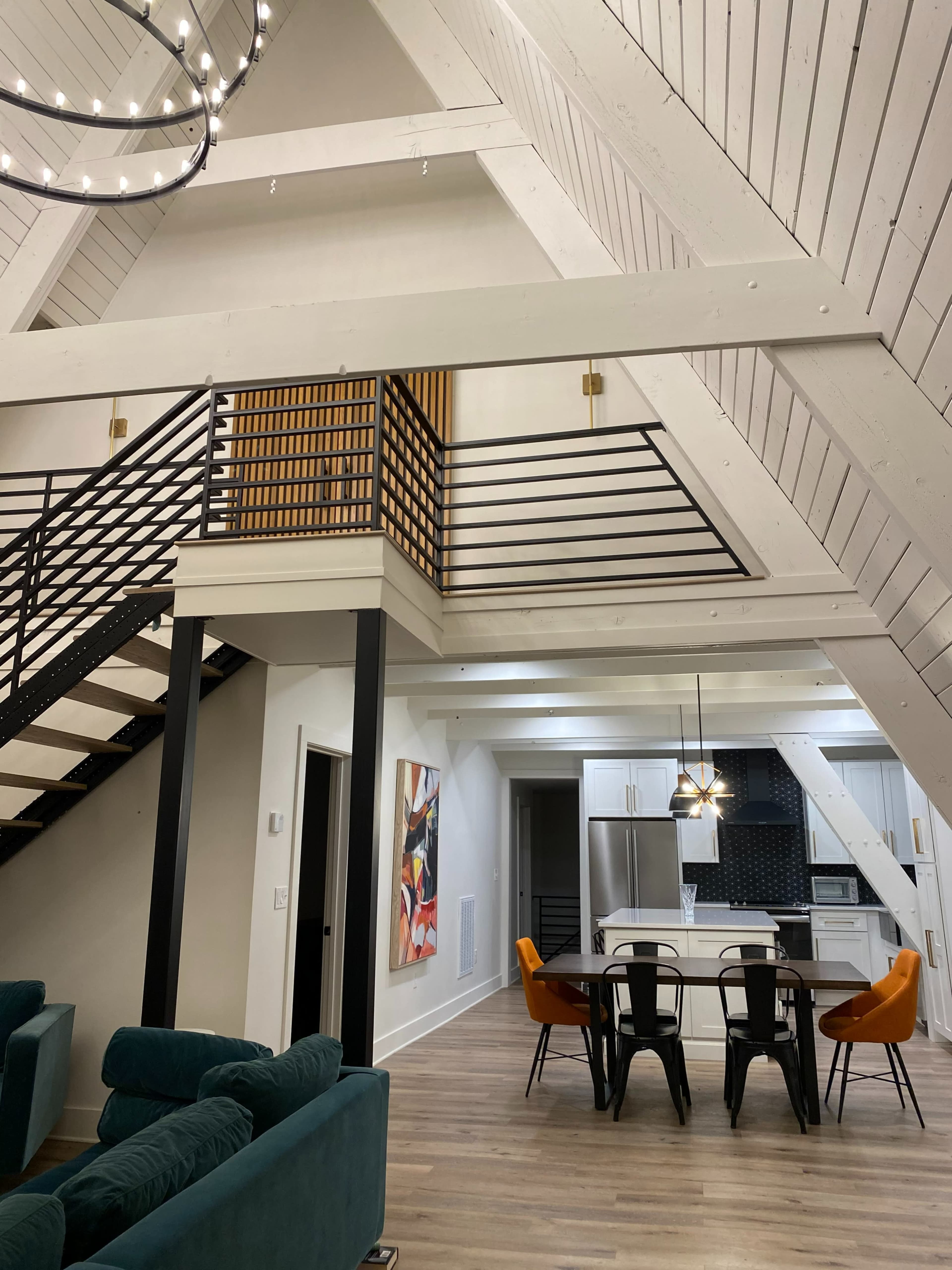 A modern, open-concept living area featuring an A-frame design with a staircase leading to a loft, a dining table, and a kitchen area.