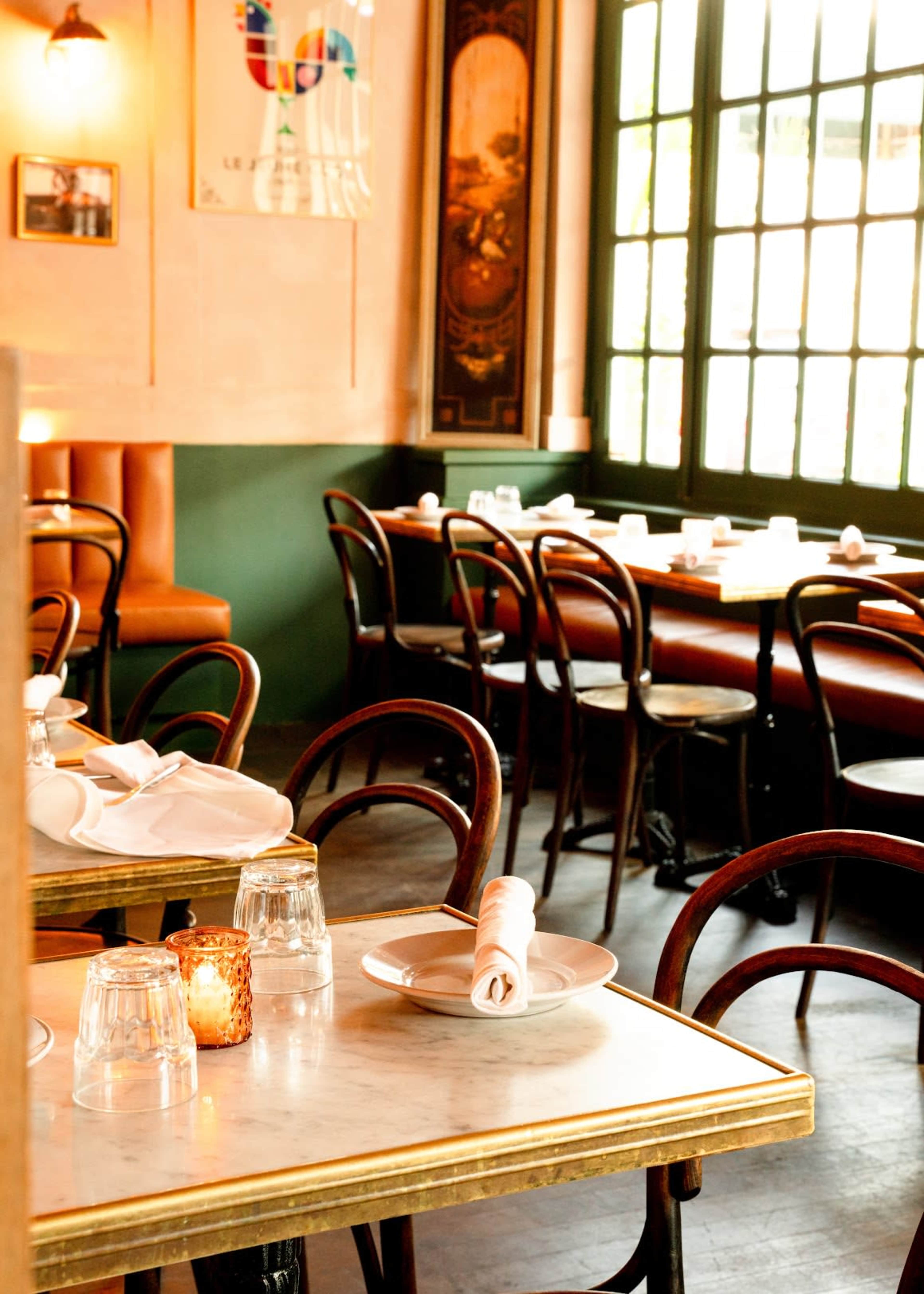 The image shows the interior of a restaurant with wooden chairs, marble-topped tables, and large windows that let in natural light.