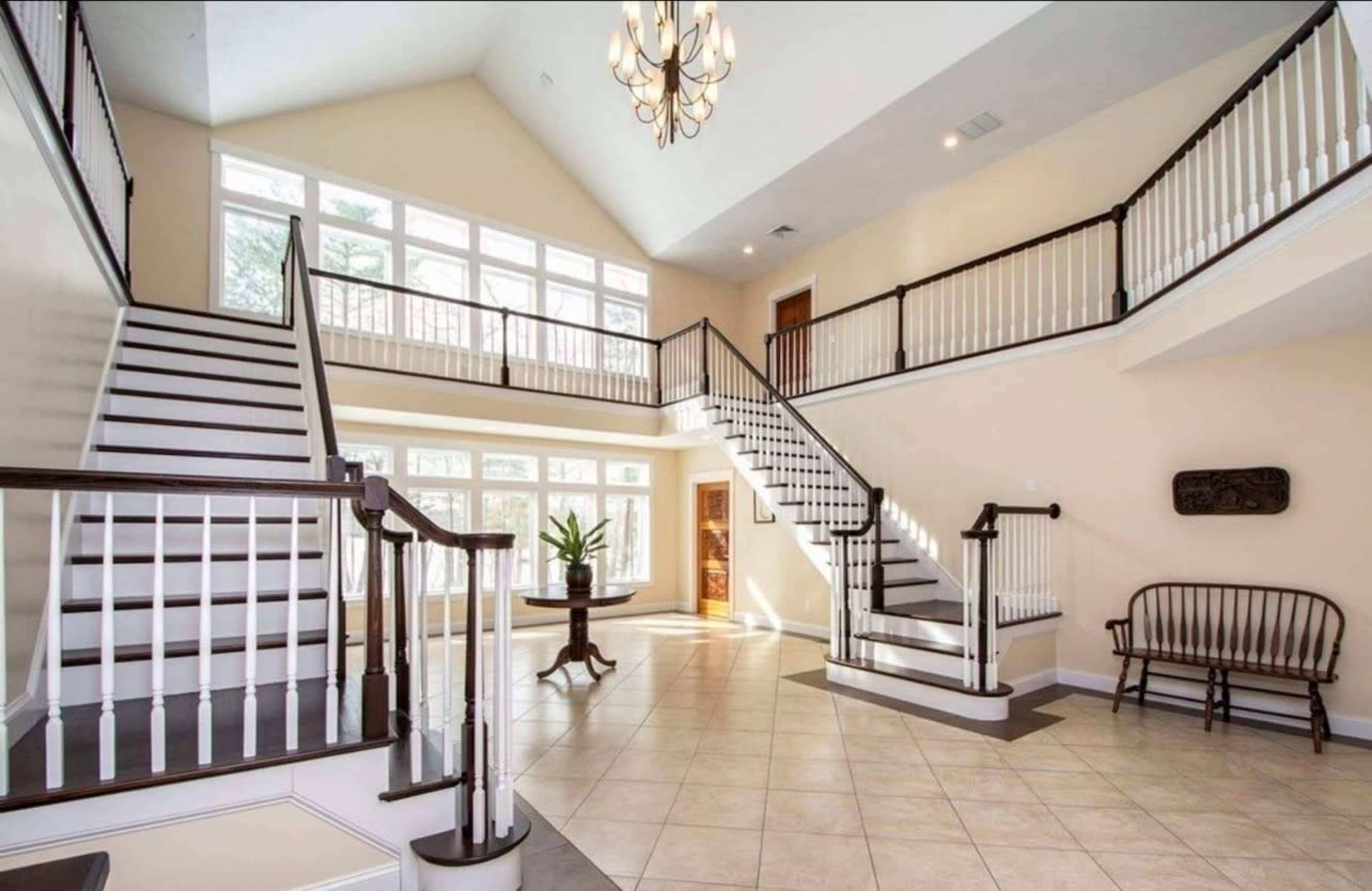 A spacious two-story entryway with large windows, sweeping staircases, and a bench by the wall.