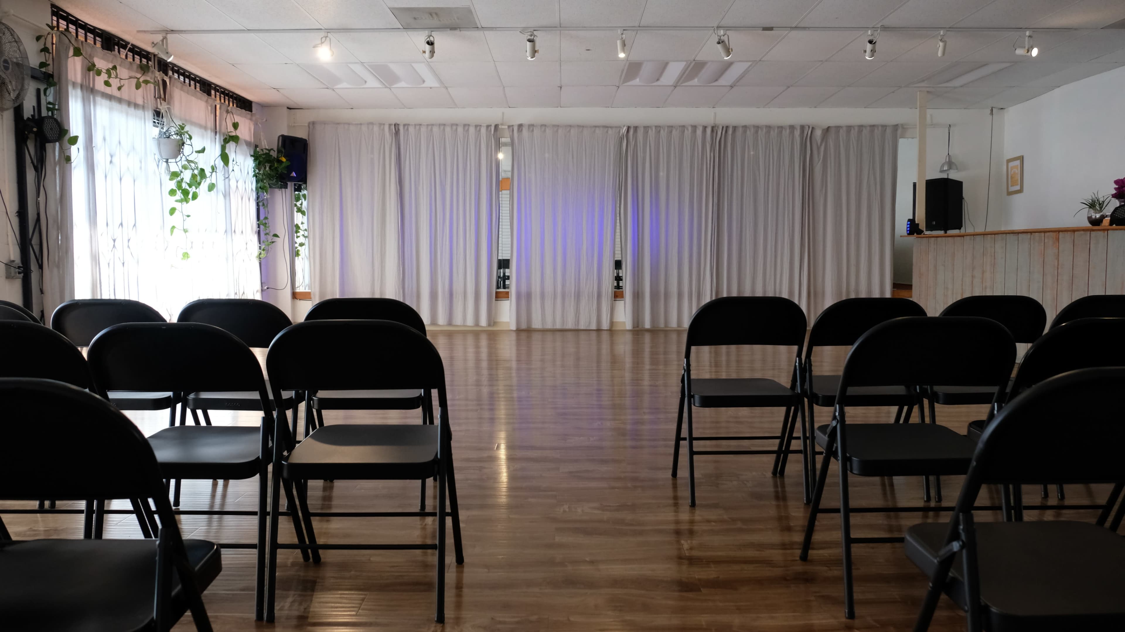 A spacious interior with rows of black folding chairs facing a white curtain backdrop in a well-lit room.