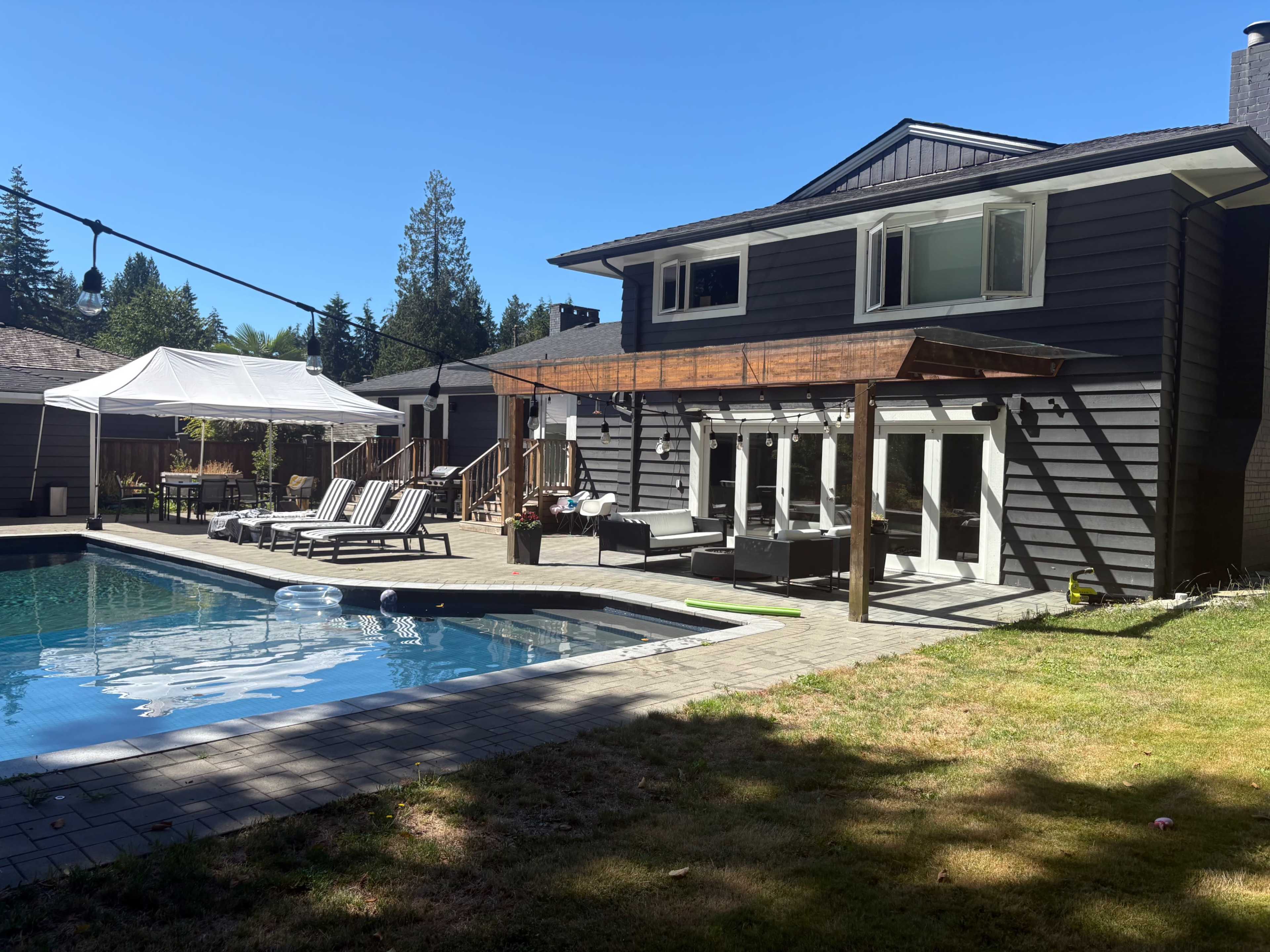 A spacious backyard features a modern home with a swimming pool surrounded by lounge chairs and a covered patio area.