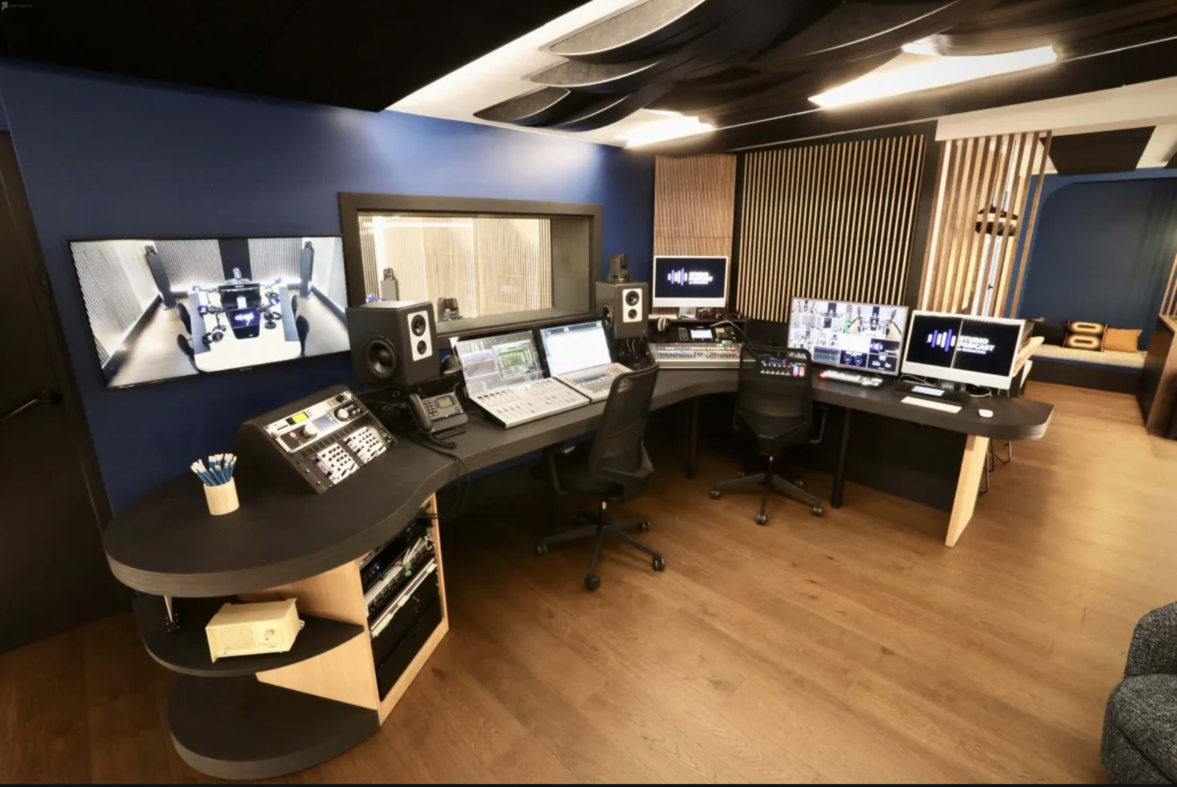 A modern audio recording studio equipped with multiple computer screens, audio mixing consoles, and soundproofing features.