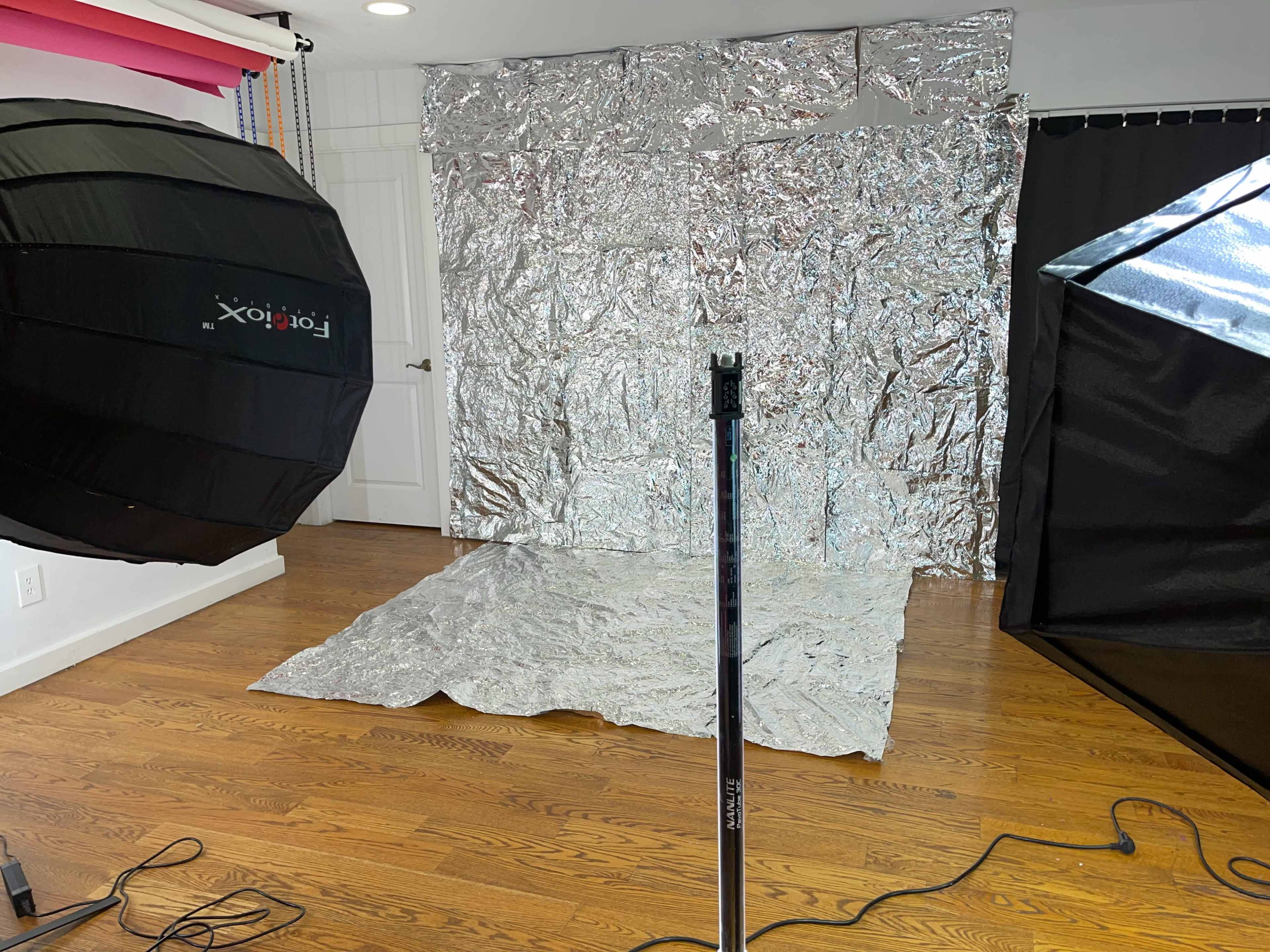 A photography studio setup with a shiny silver backdrop and two light sources positioned on either side.