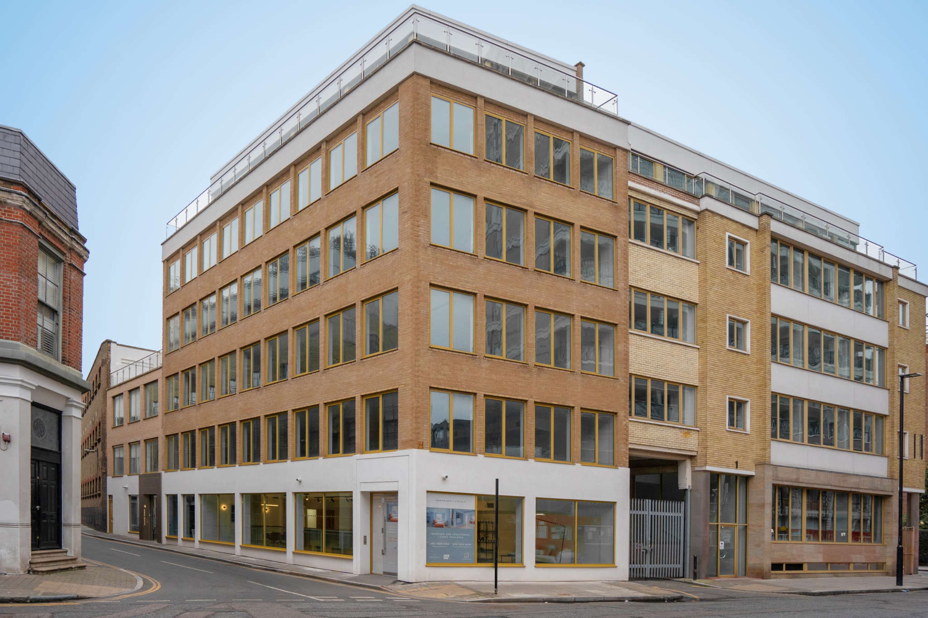 A modern, four-story brick building with large windows is situated at the corner of a street.