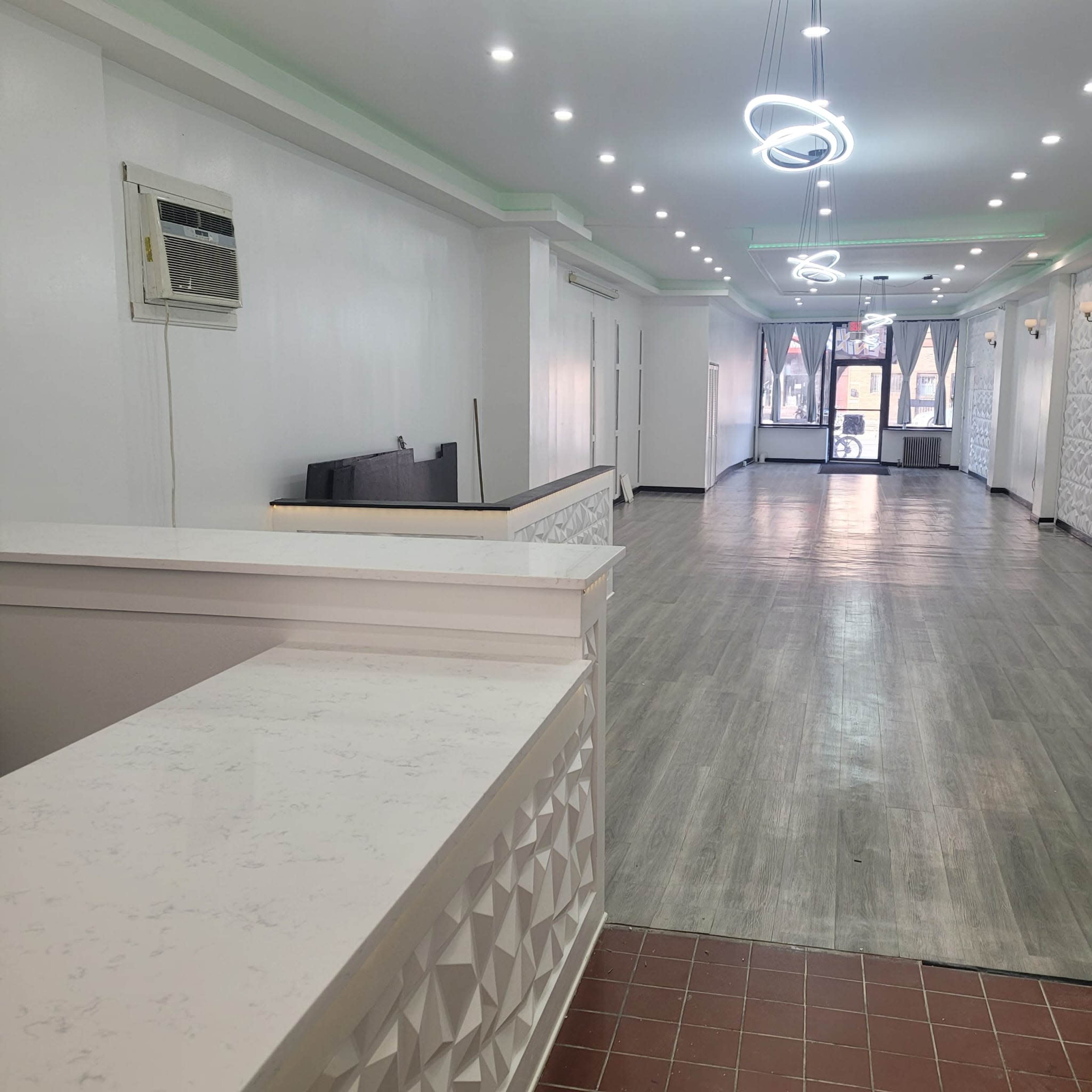 The image shows a spacious, well-lit interior with a reception area and smooth flooring leading toward an entrance with large windows.