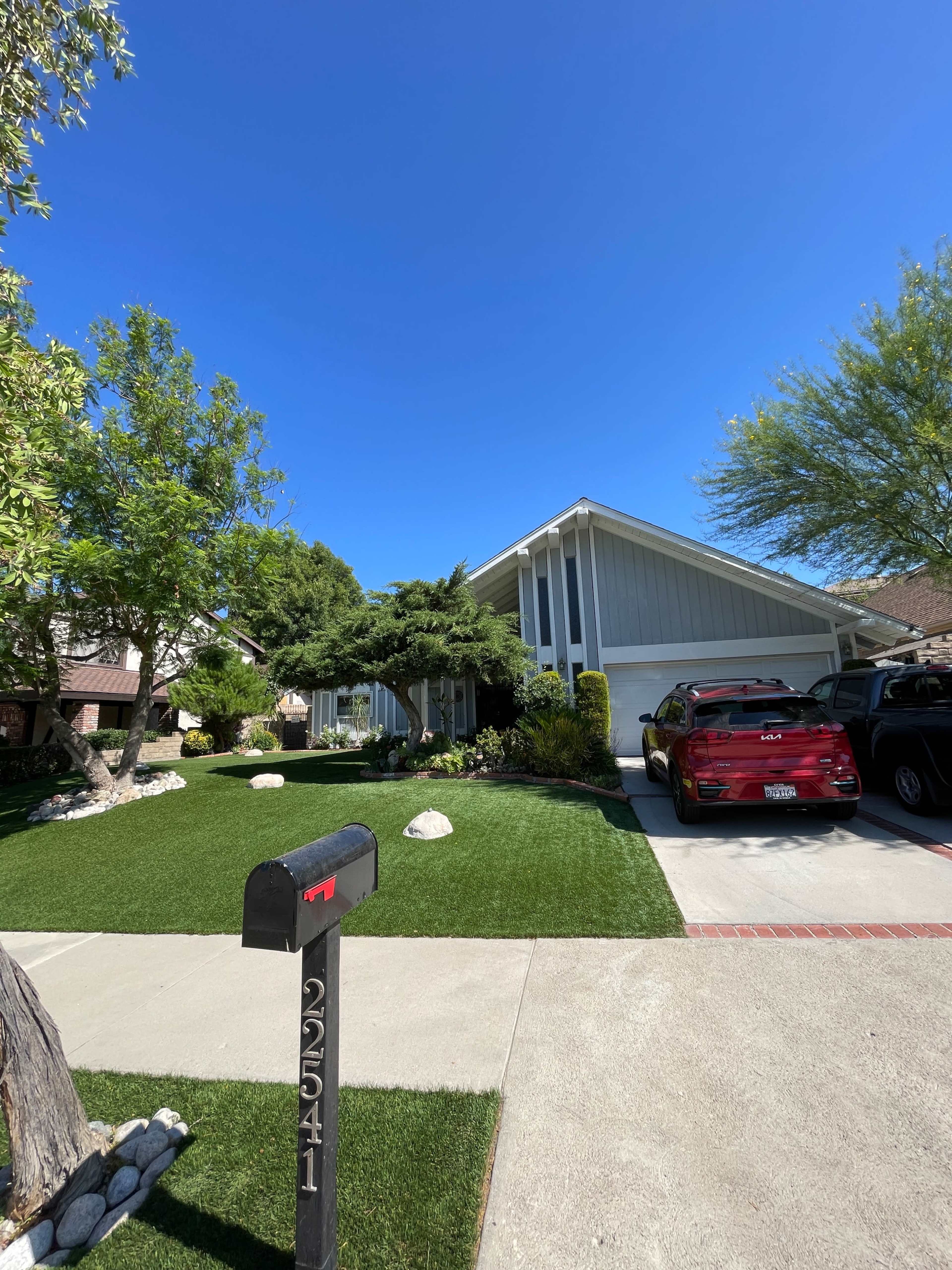 A well-maintained suburban front yard features a mailbox, manicured grass, and a contemporary house with a driveway for parked cars.
