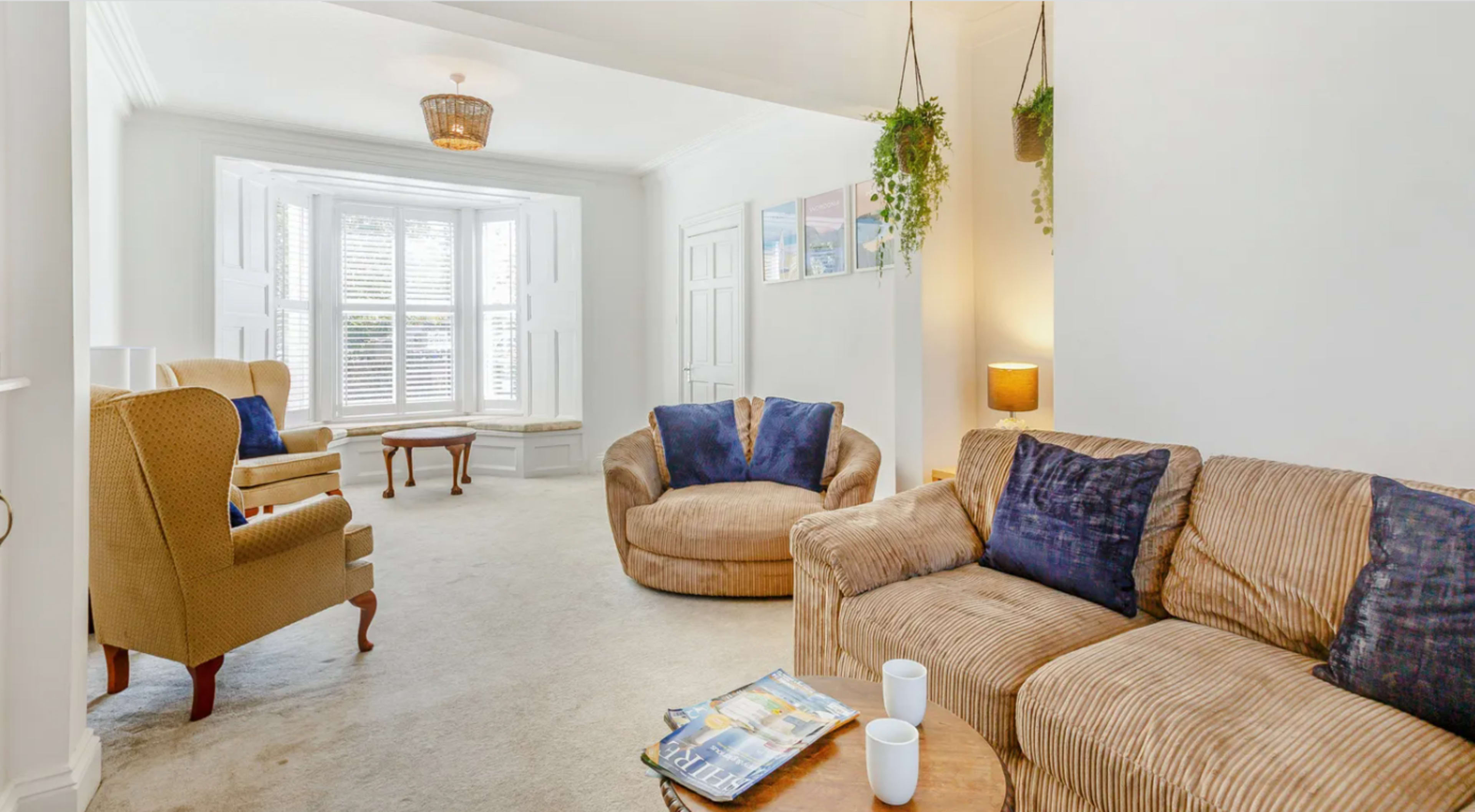 A living room with two armchairs, a round coffee table, and a sectional couch, all set against white walls and a large bay window.
