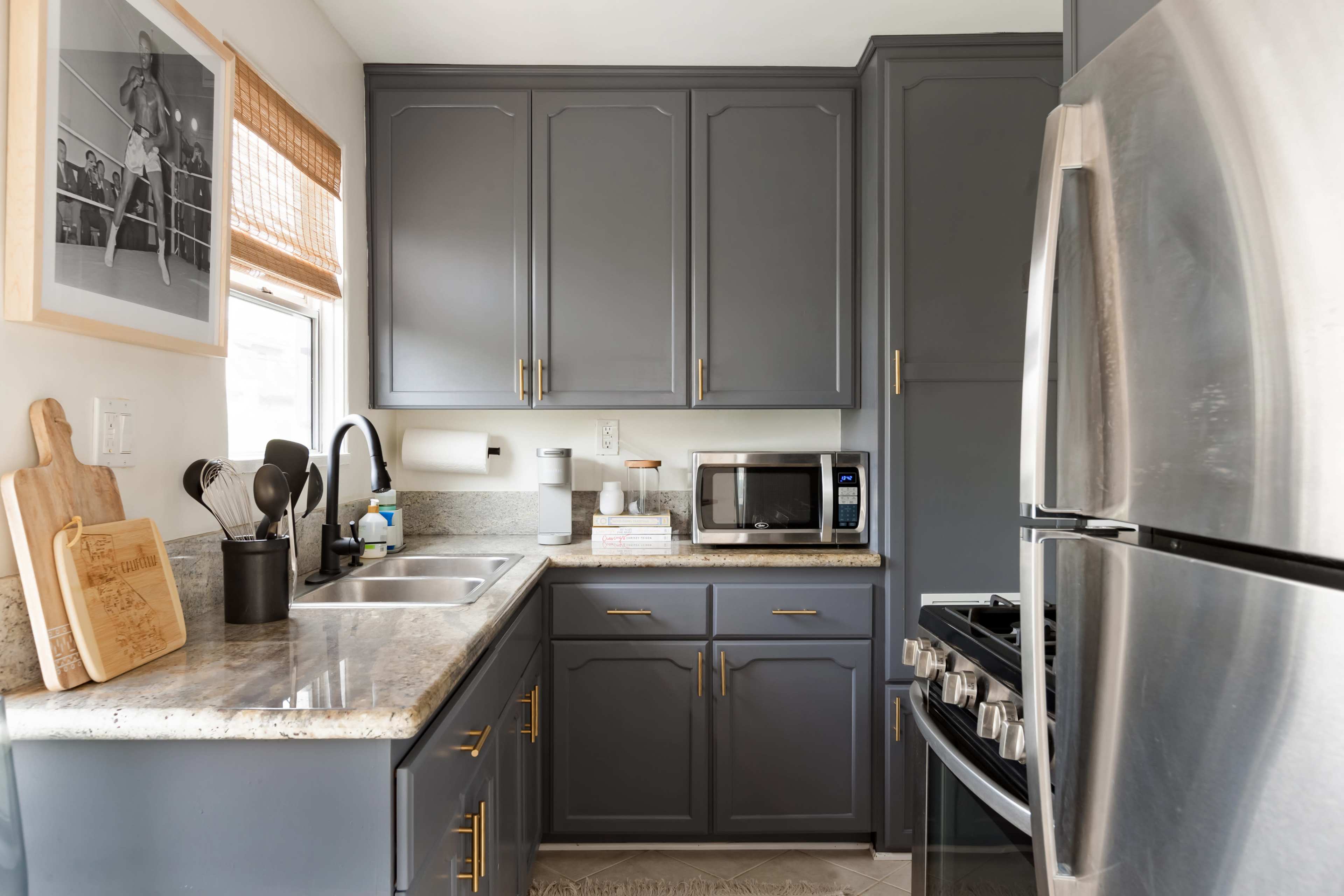 A compact kitchen with gray cabinets, stainless steel appliances, and a granite countertop.