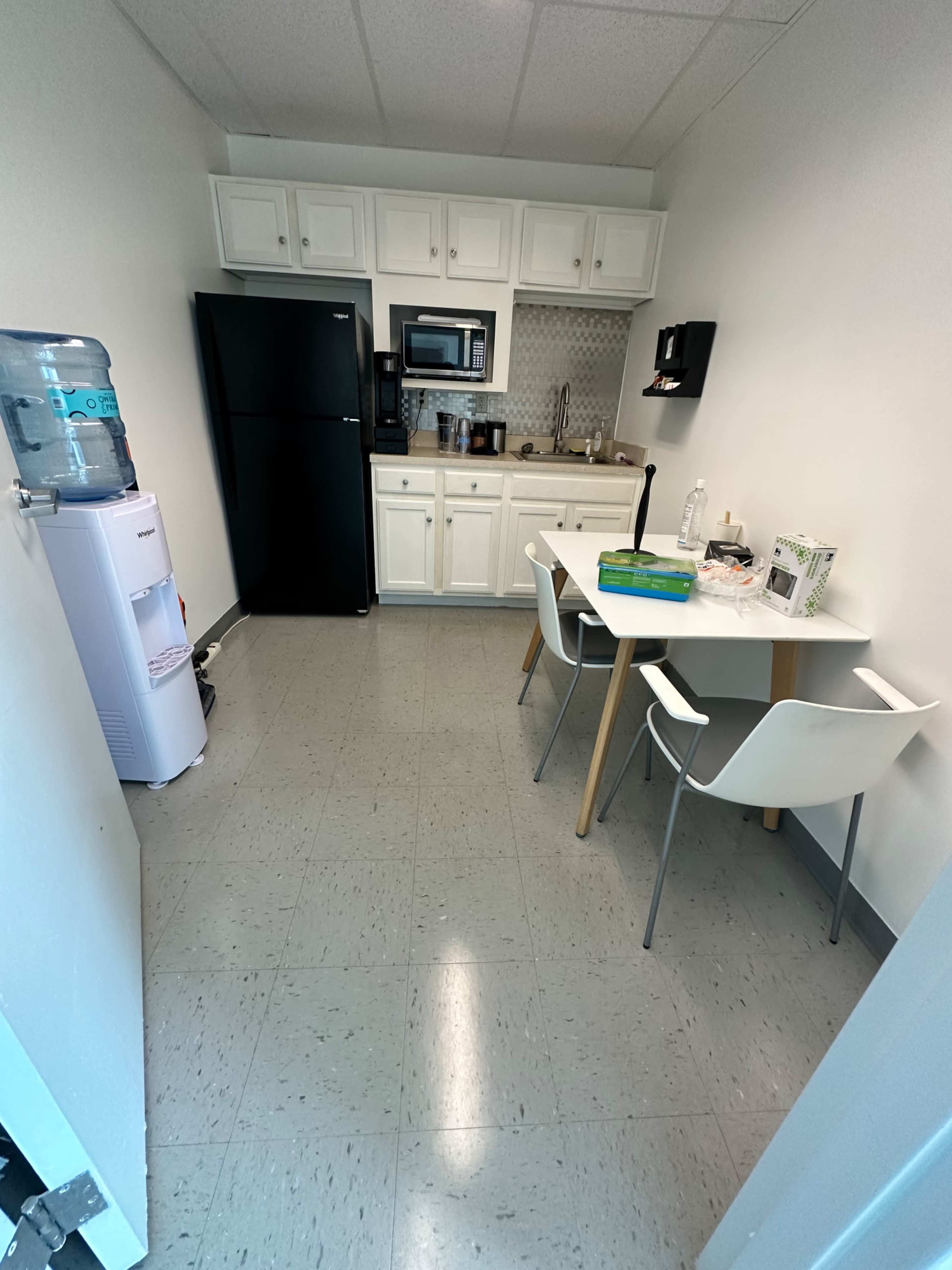 A small kitchen area featuring a black refrigerator, a microwave, a table with two chairs, and a water cooler.