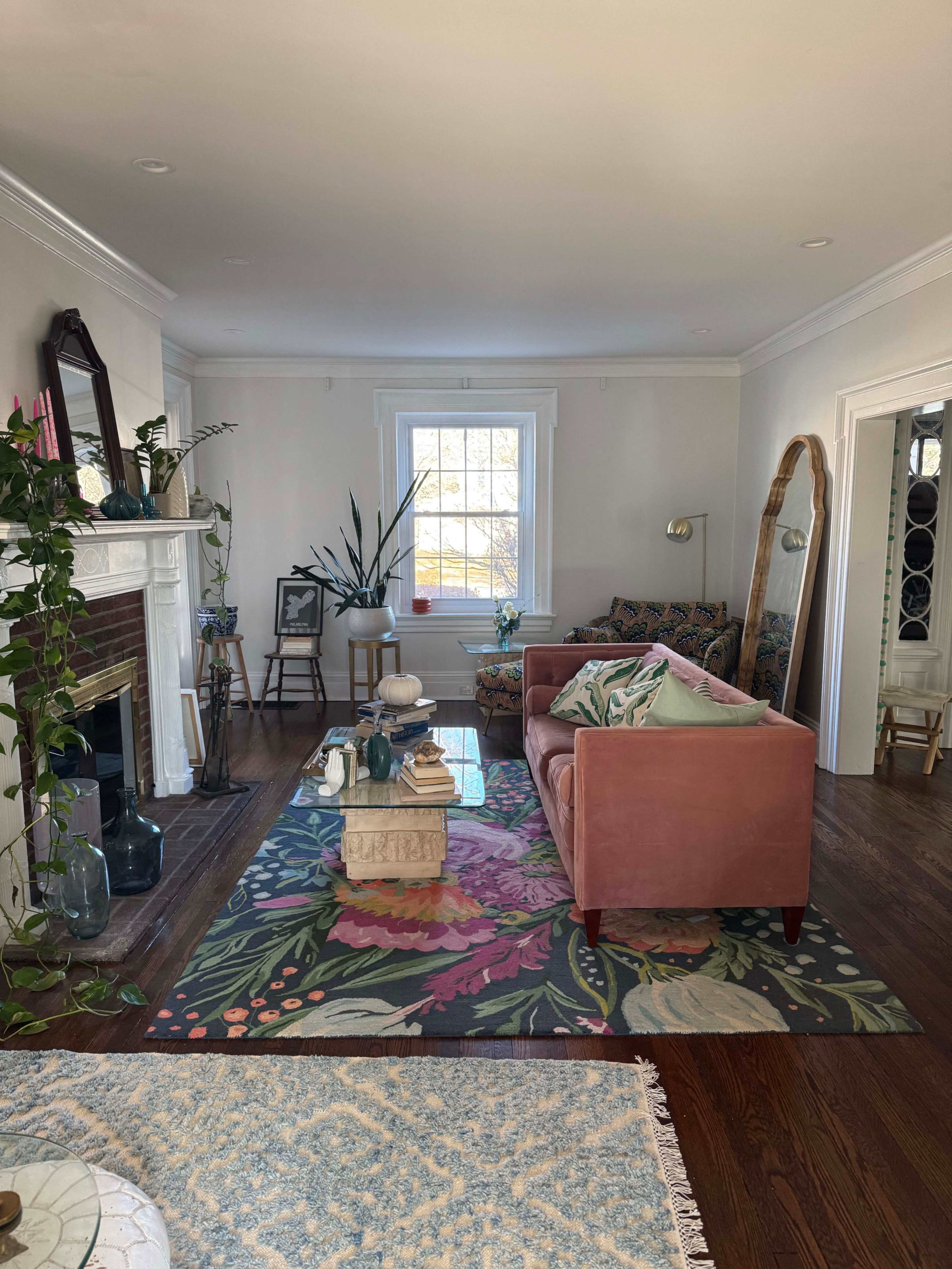 The living room features a pink sofa, a large patterned rug, and a decorative fireplace, with plants and artwork enhancing the decor.