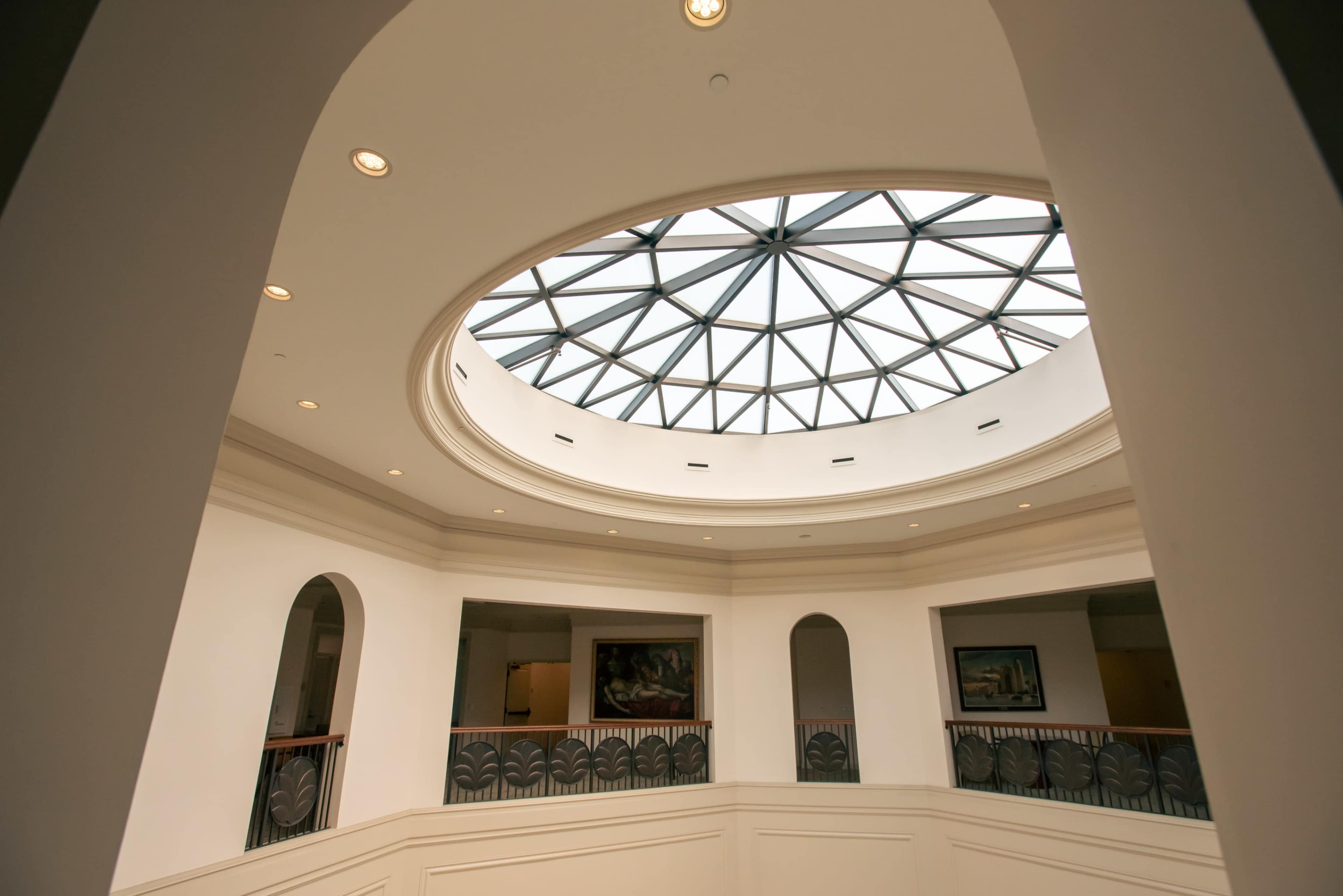 A circular skylight with a geometric design illuminates a multi-level atrium featuring curved walls and decorative railings.