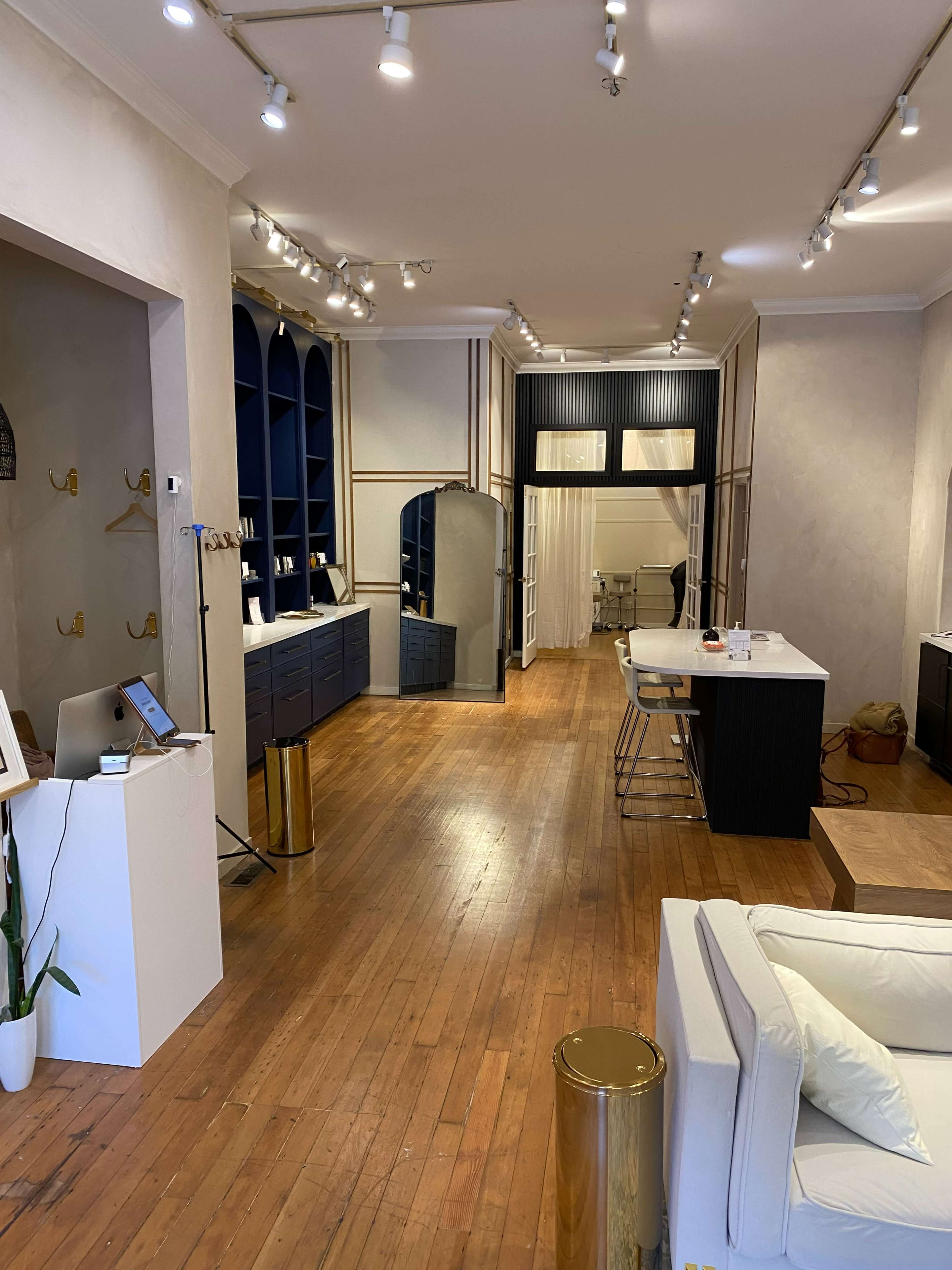 The image shows a spacious boutique interior featuring wooden flooring, contemporary furniture, and stylish shelving displays.