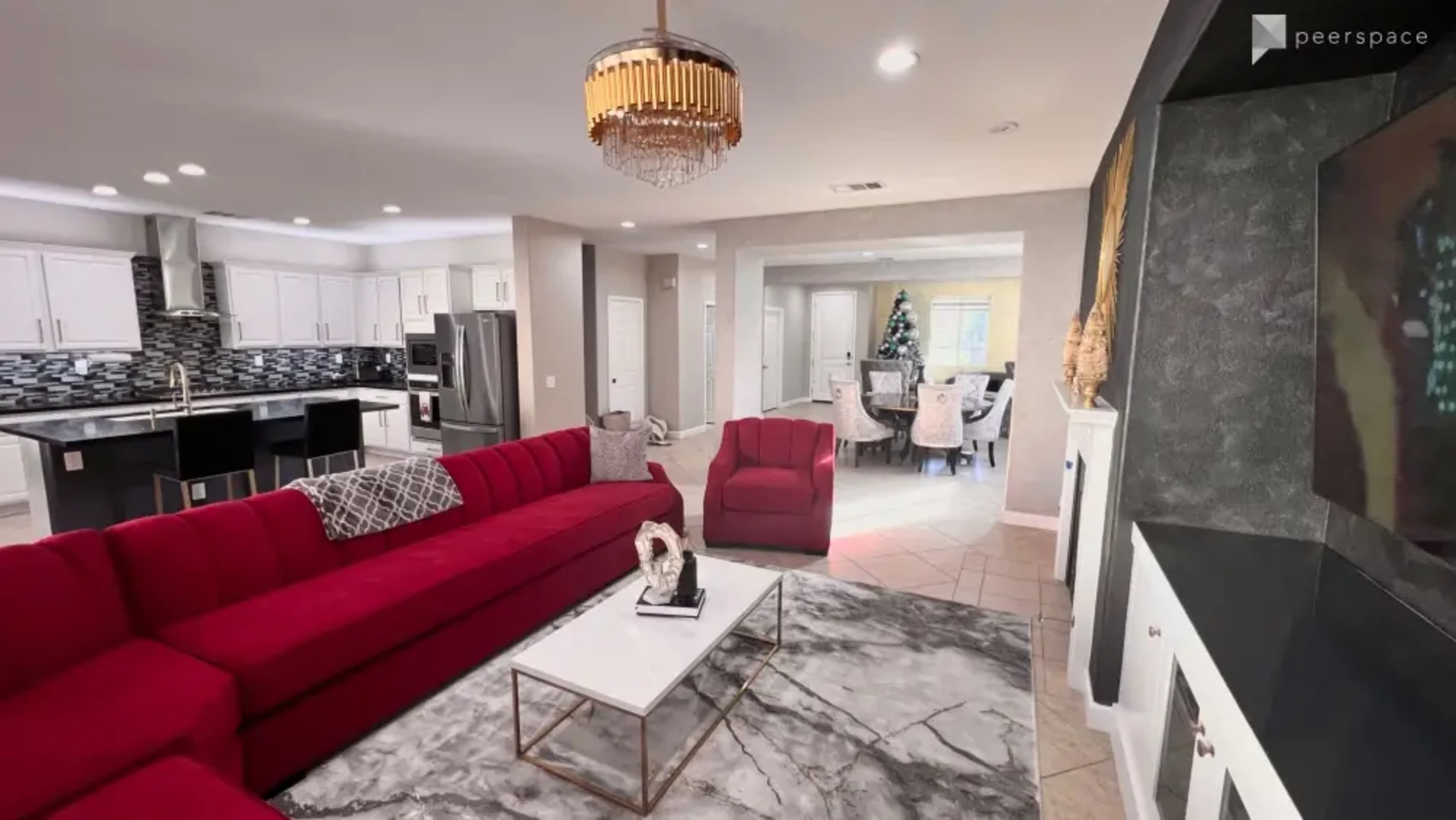 The image shows a modern living room featuring a red sectional sofa, a marble coffee table, and a view of an adjacent dining area decorated for the holidays.