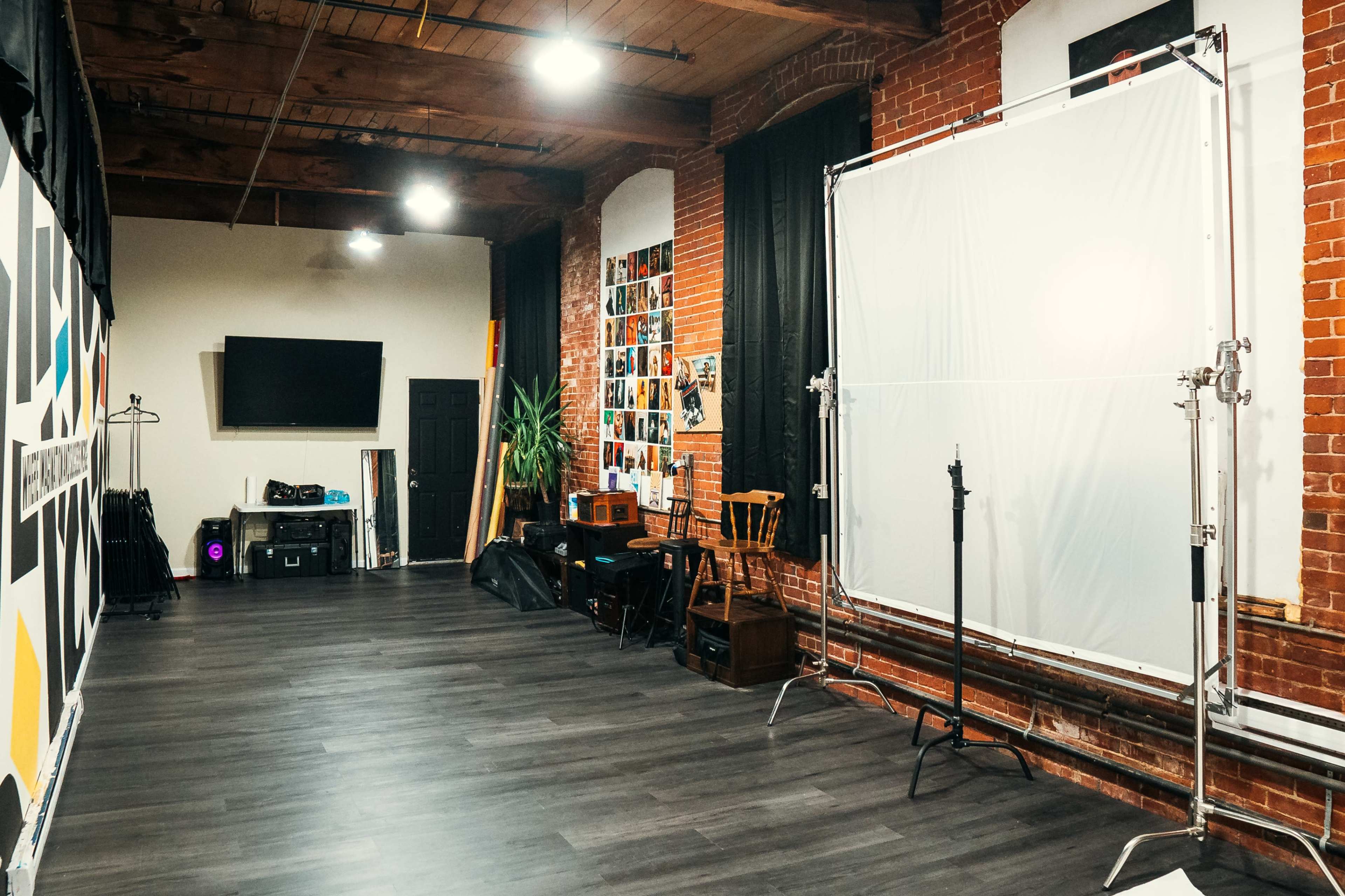 A spacious studio with brick walls features a large white backdrop, wooden flooring, and various equipment arranged along one side.