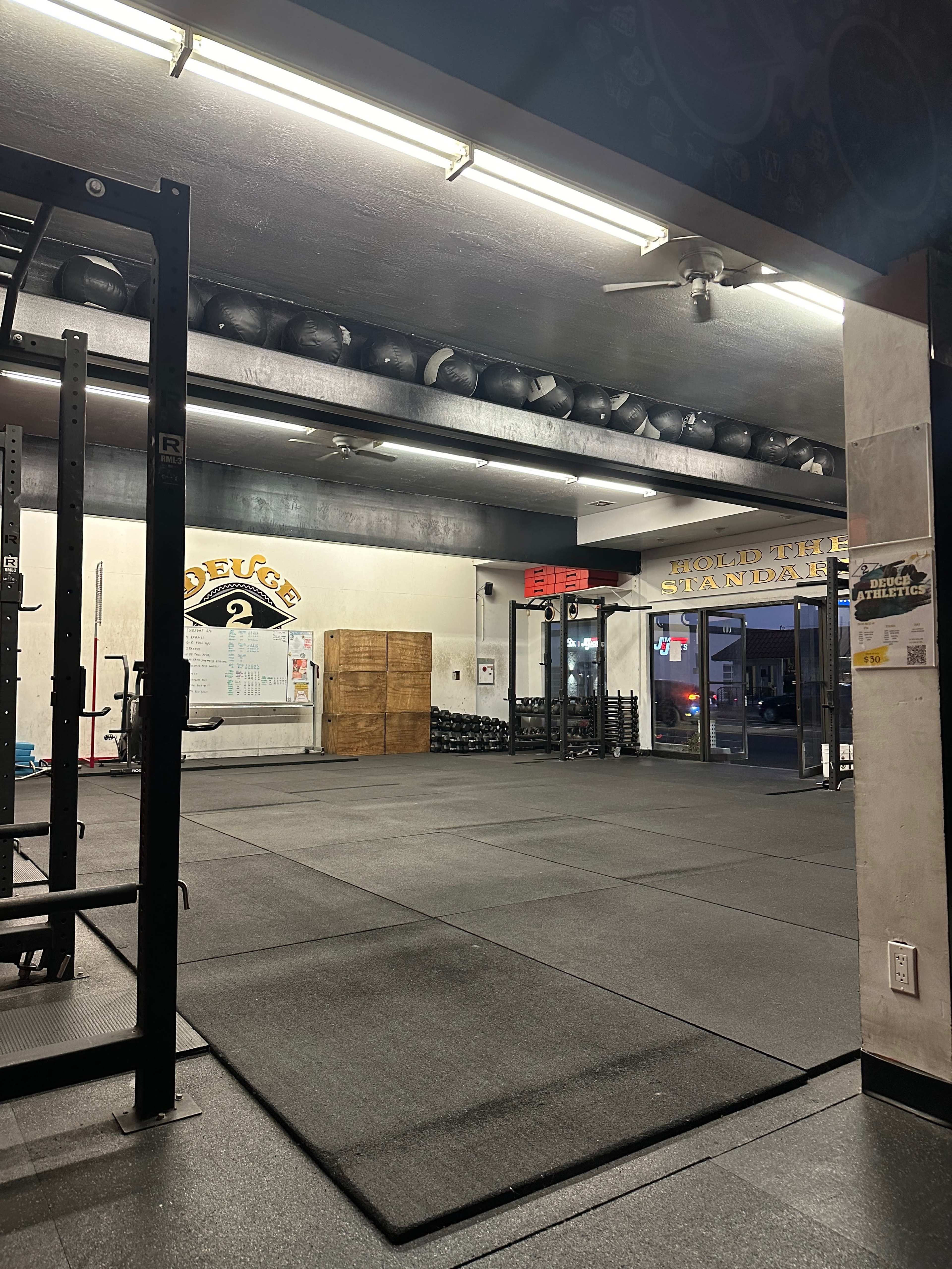 A gym interior featuring weightlifting equipment, storage spaces for exercise balls, and a spacious workout area with rubber flooring.