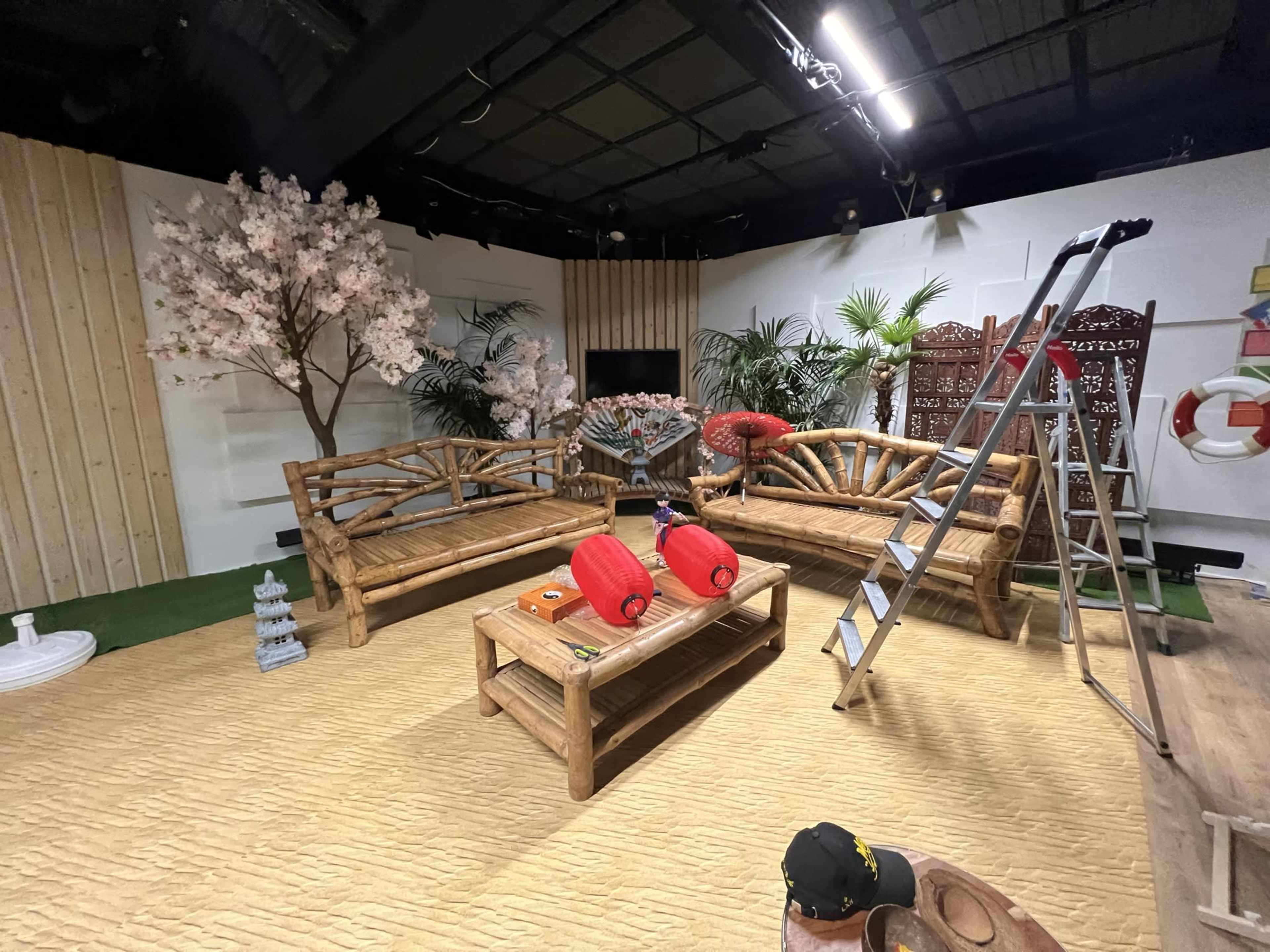 The scene features a cozy indoor space with wooden furniture, a decorative table in the center, pink cherry blossom trees, and a ladder against the wall.