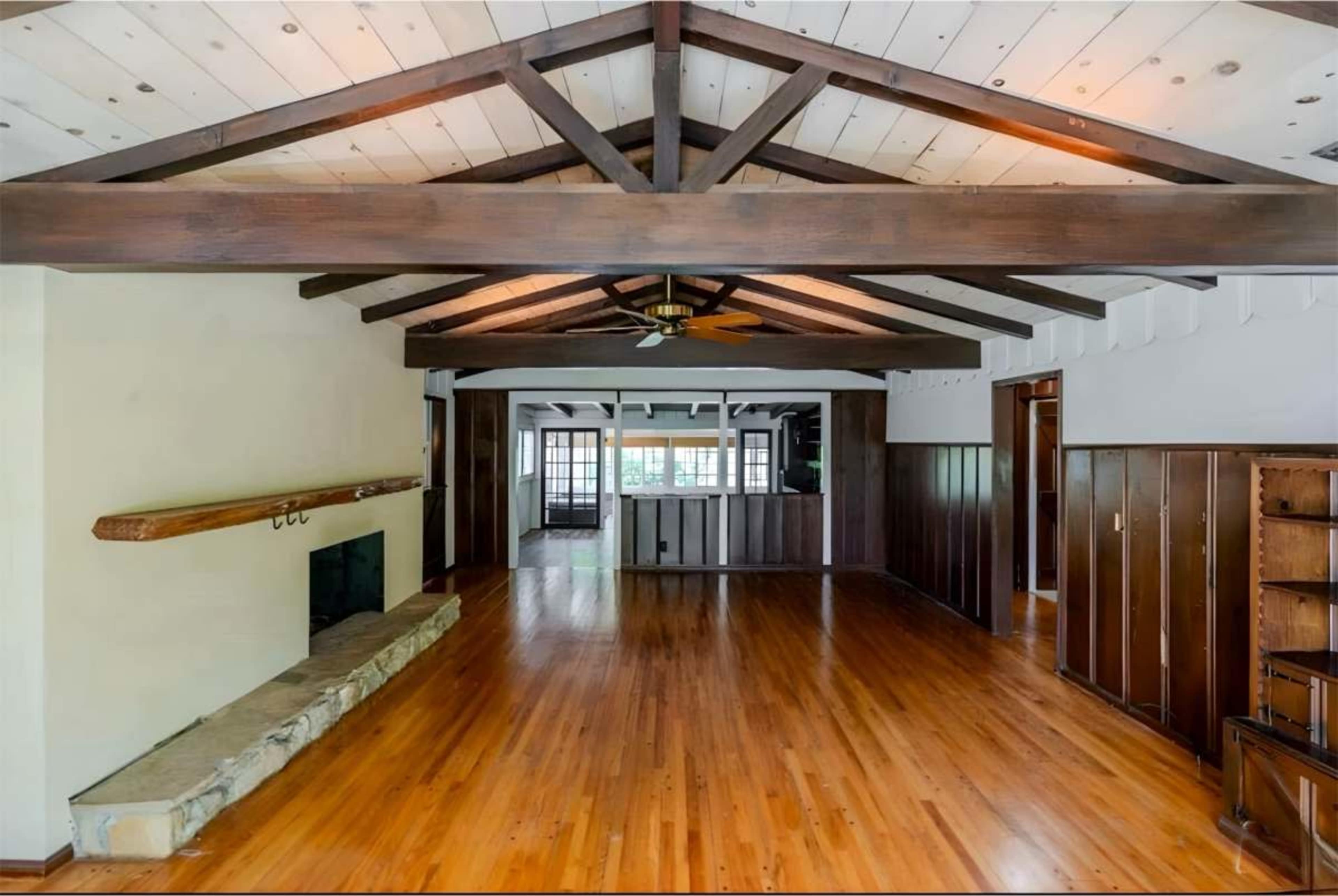 An open interior space with wooden beams, a stone fireplace, and hardwood floors.