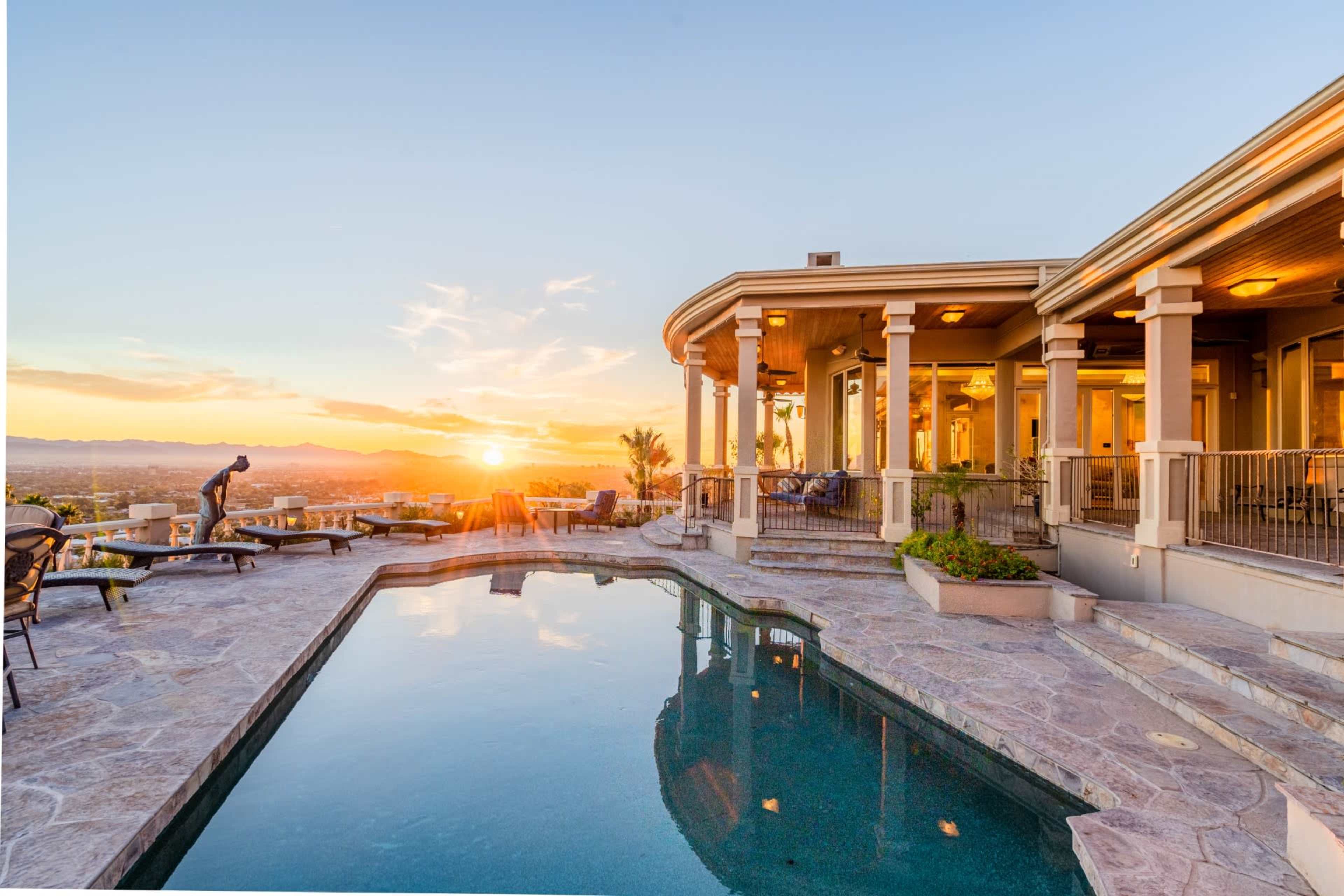 A luxurious backyard features a swimming pool and a sunset view over the mountains.