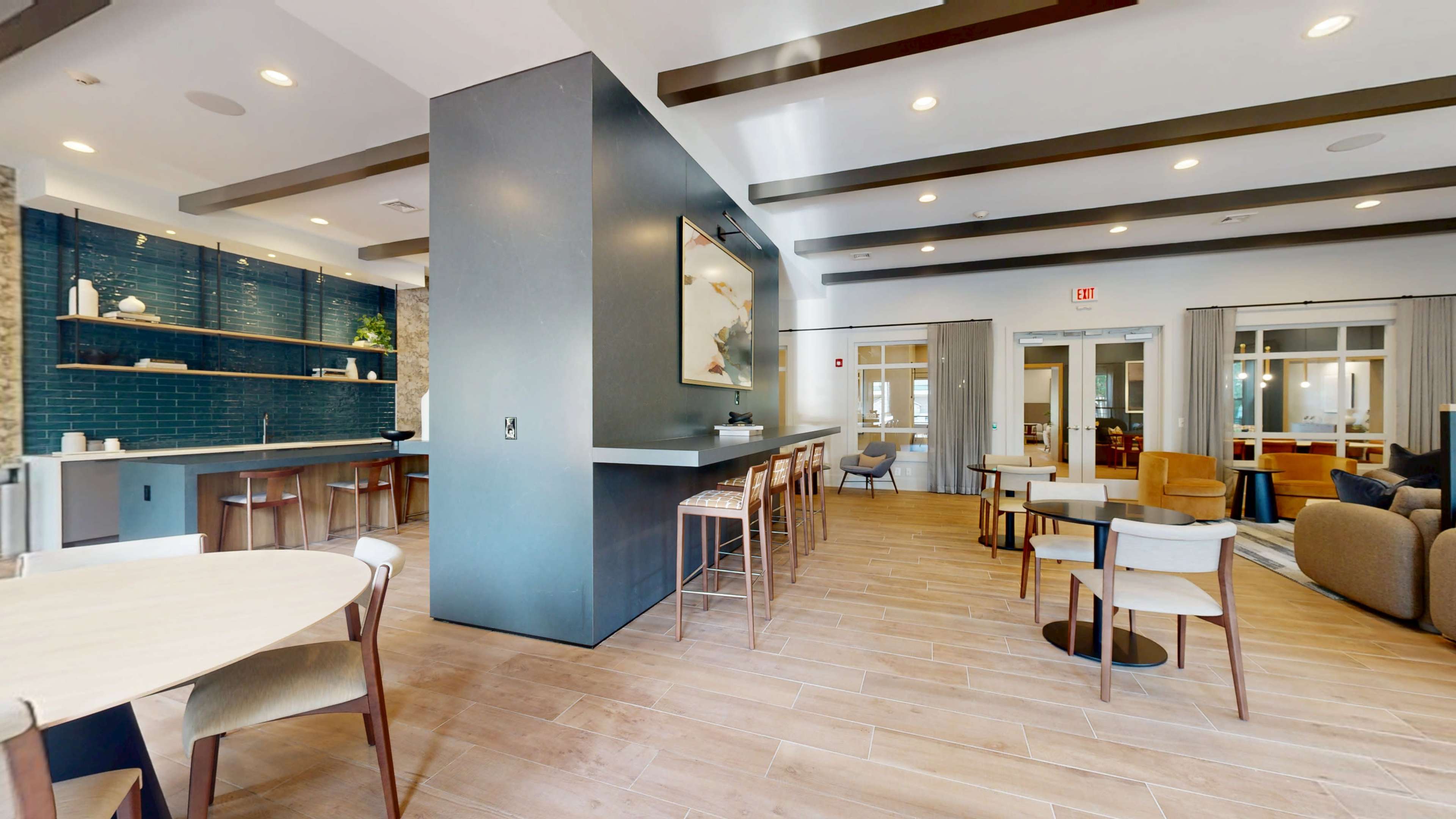 The image shows a modern interior of a community space featuring a mix of seating options, a bar area, and natural lighting.