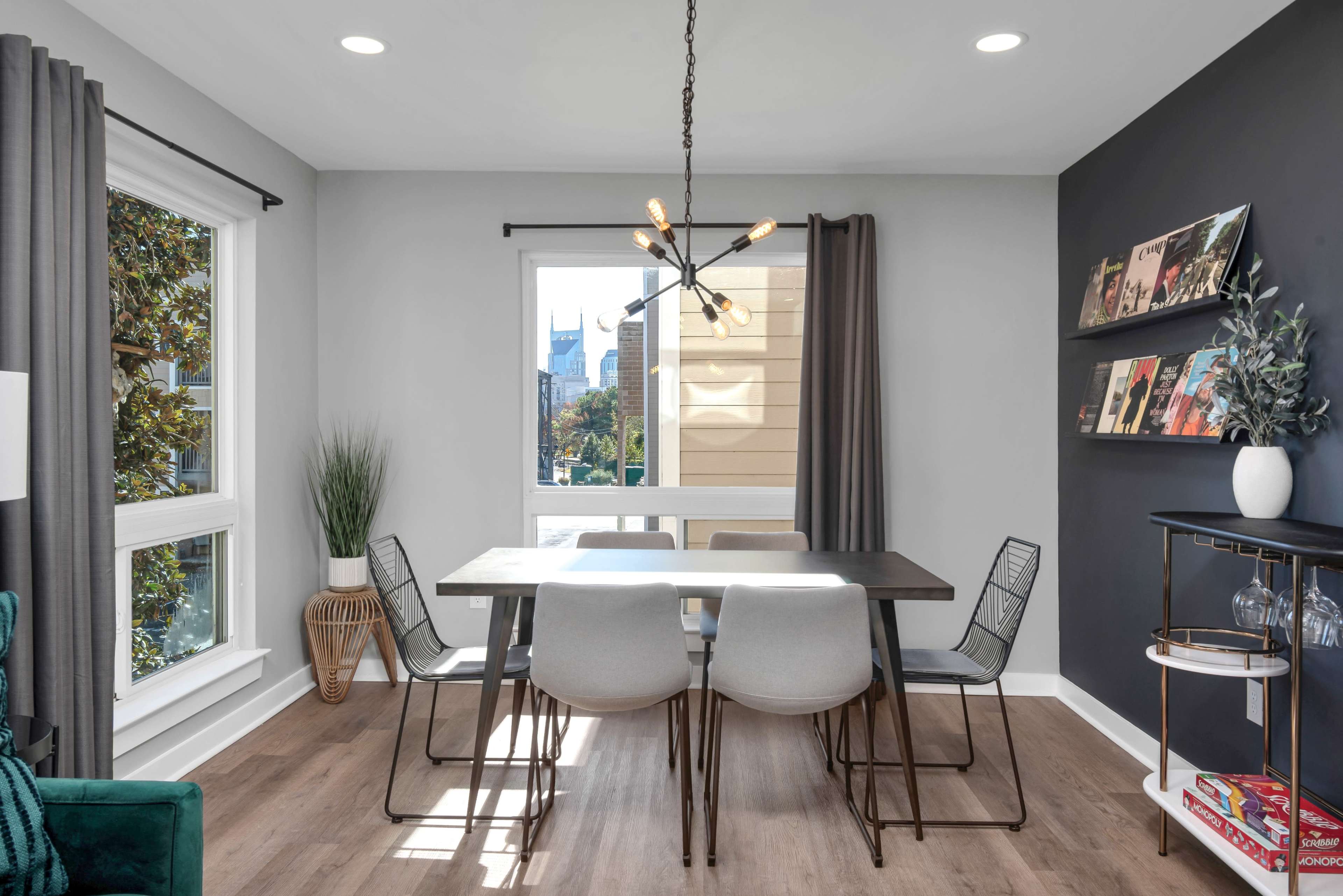 The image shows a modern dining area with a rectangular table surrounded by six chairs, a window with a view, and minimalist decor including a pendant light and wall shelves.