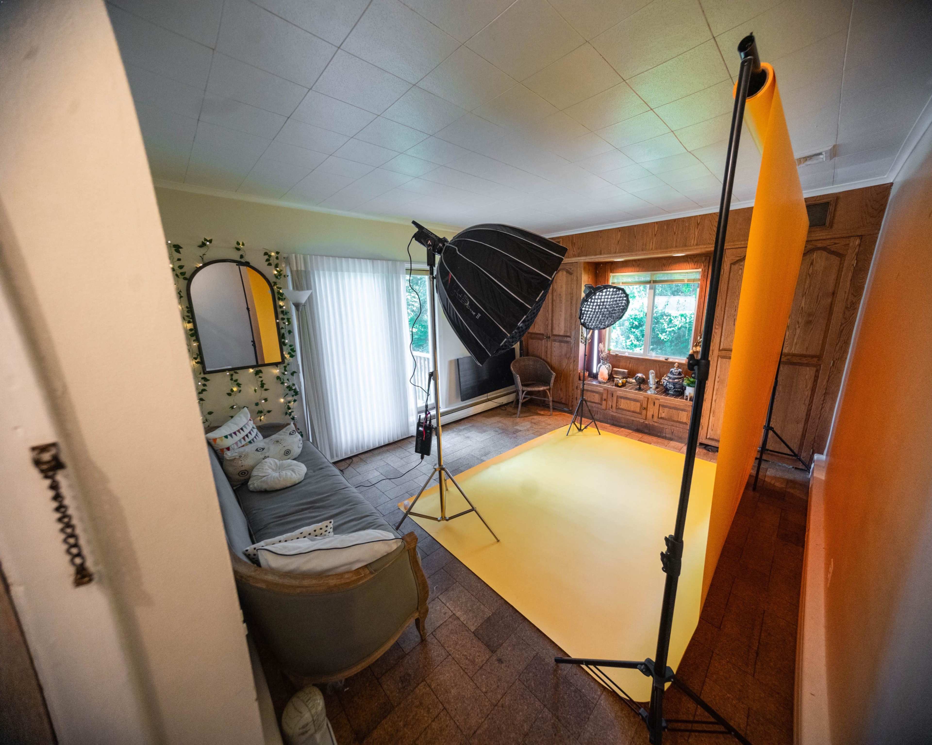 A photography studio setup features a yellow backdrop, lighting equipment, and a seating area within a spacious living room.