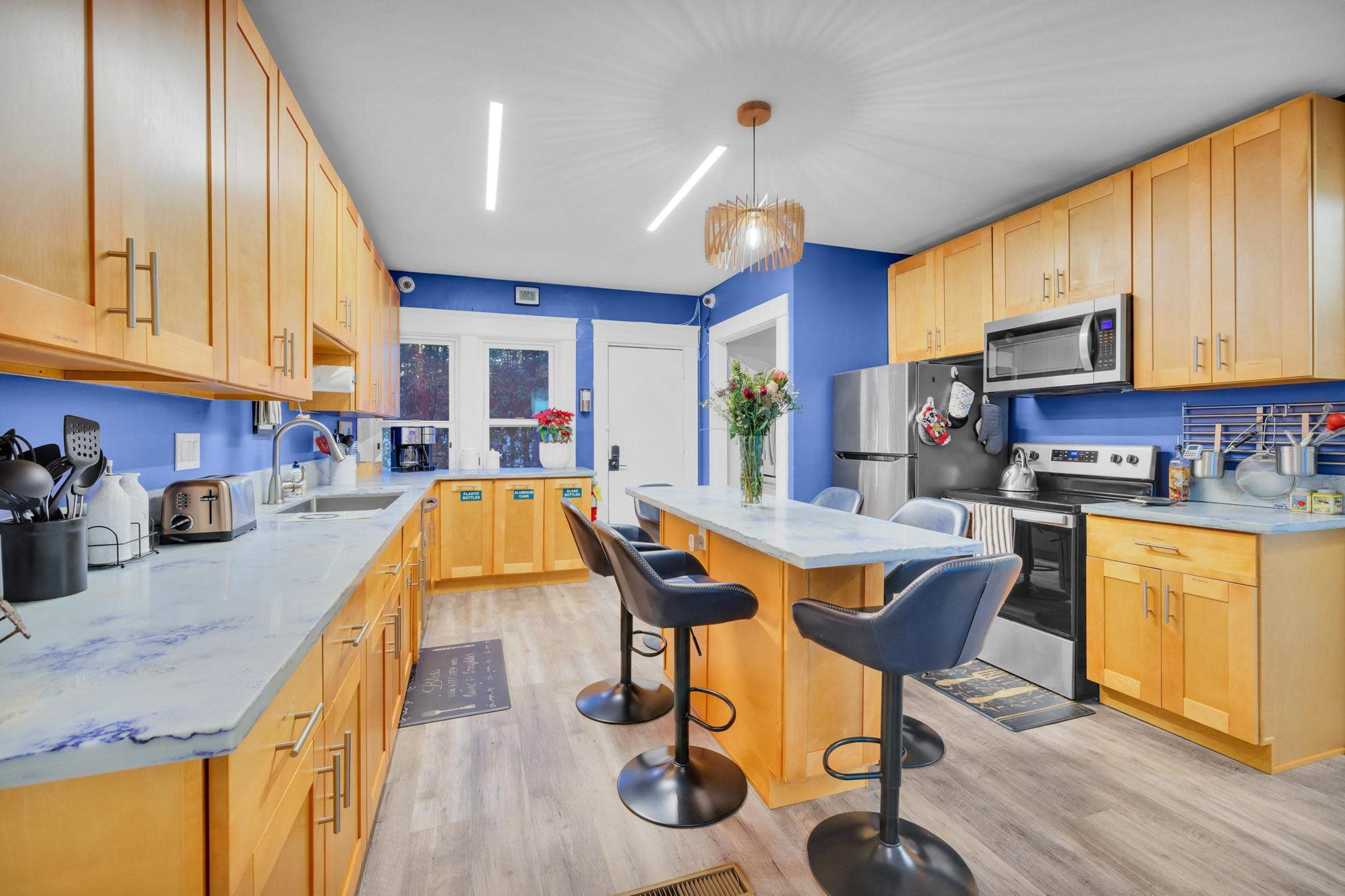 A modern kitchen featuring blue walls, wooden cabinetry, a central island with seating, and stainless steel appliances.