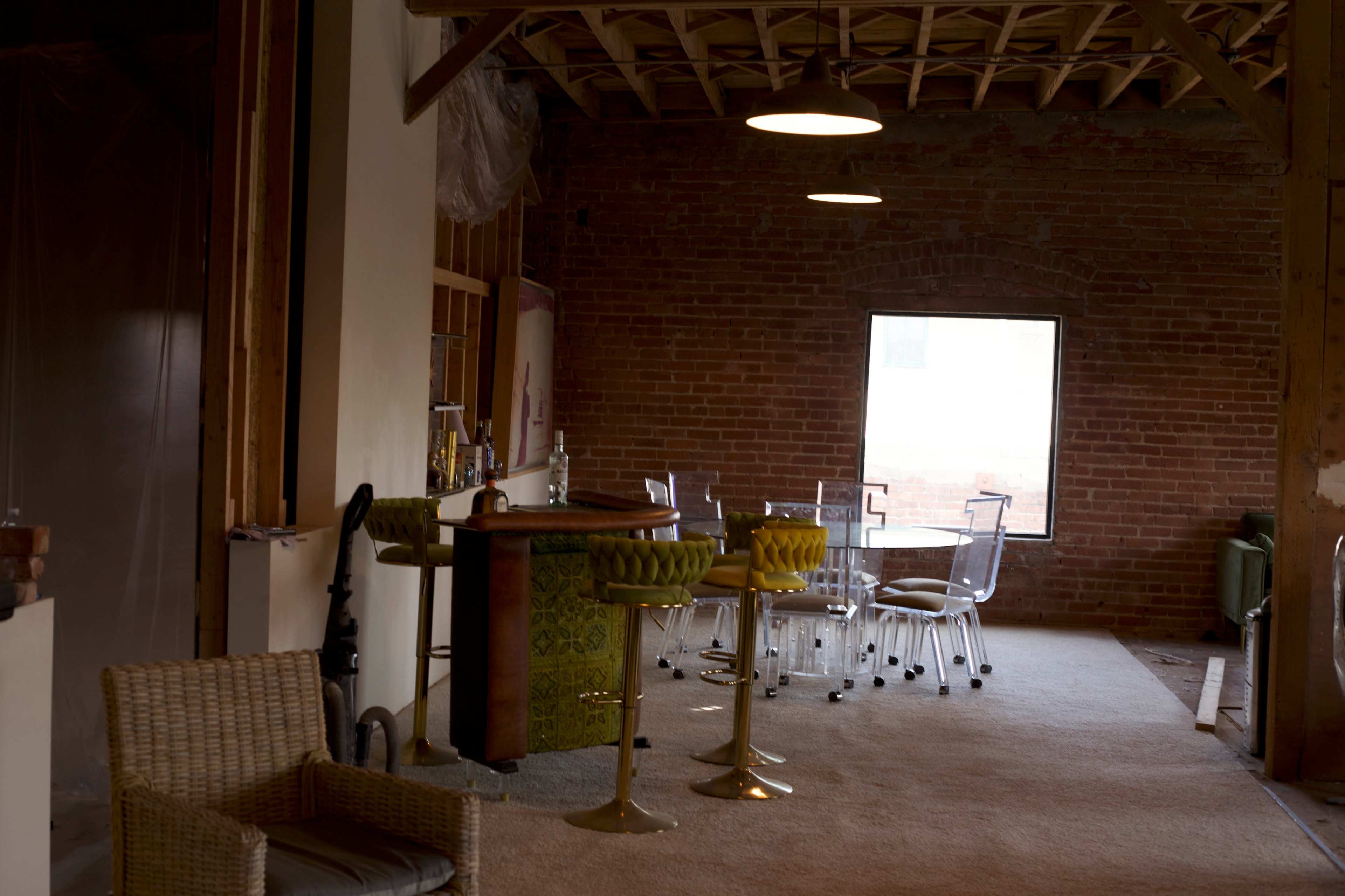 An unfinished interior space with brick walls, a bar area, and a table surrounded by transparent chairs.