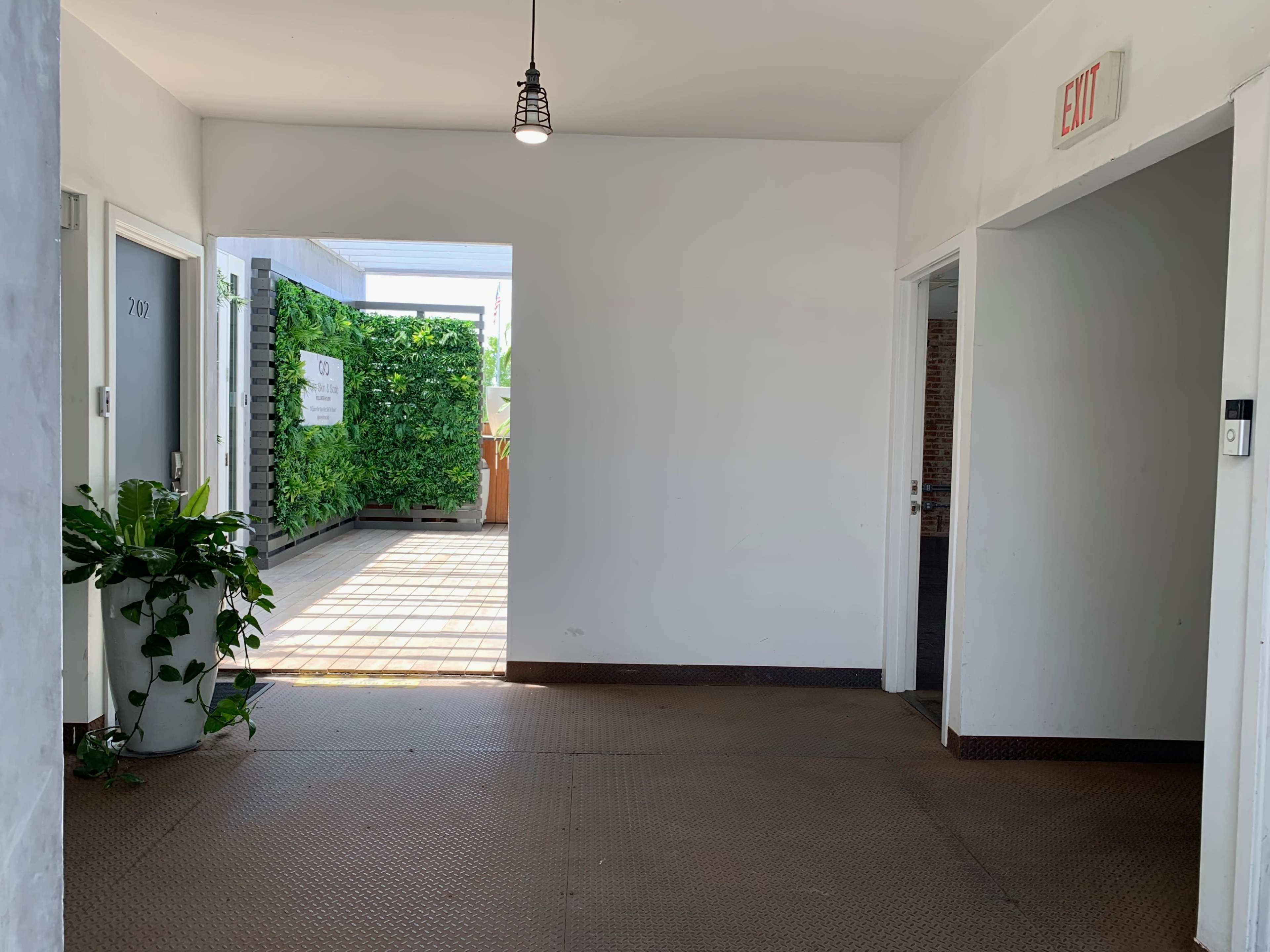 A bright hallway with doors on either side, leading to a green outdoor area visible at the end.