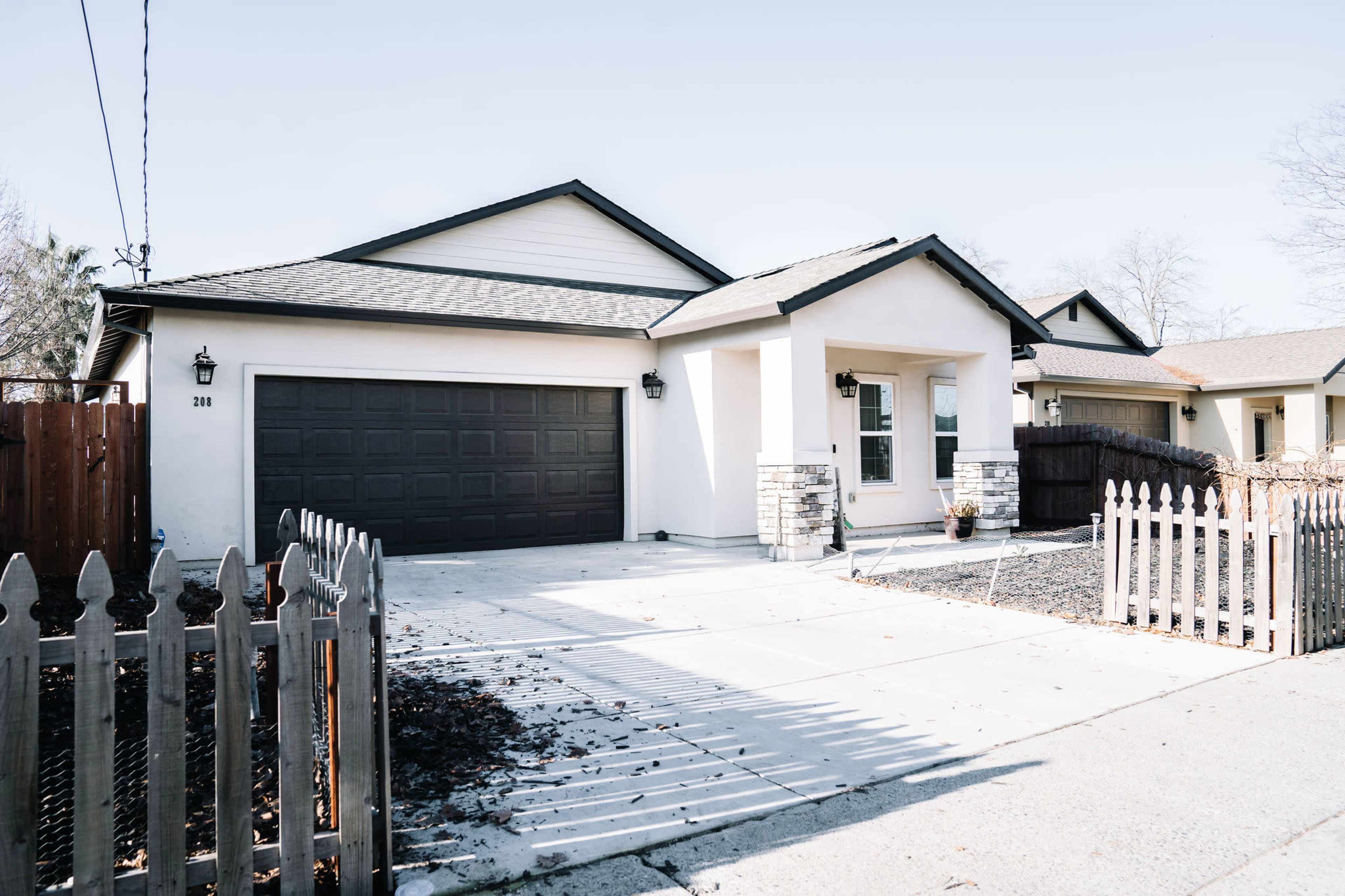 A single-story residential house with a gray garage door, a light-colored exterior, and a neatly landscaped front yard.