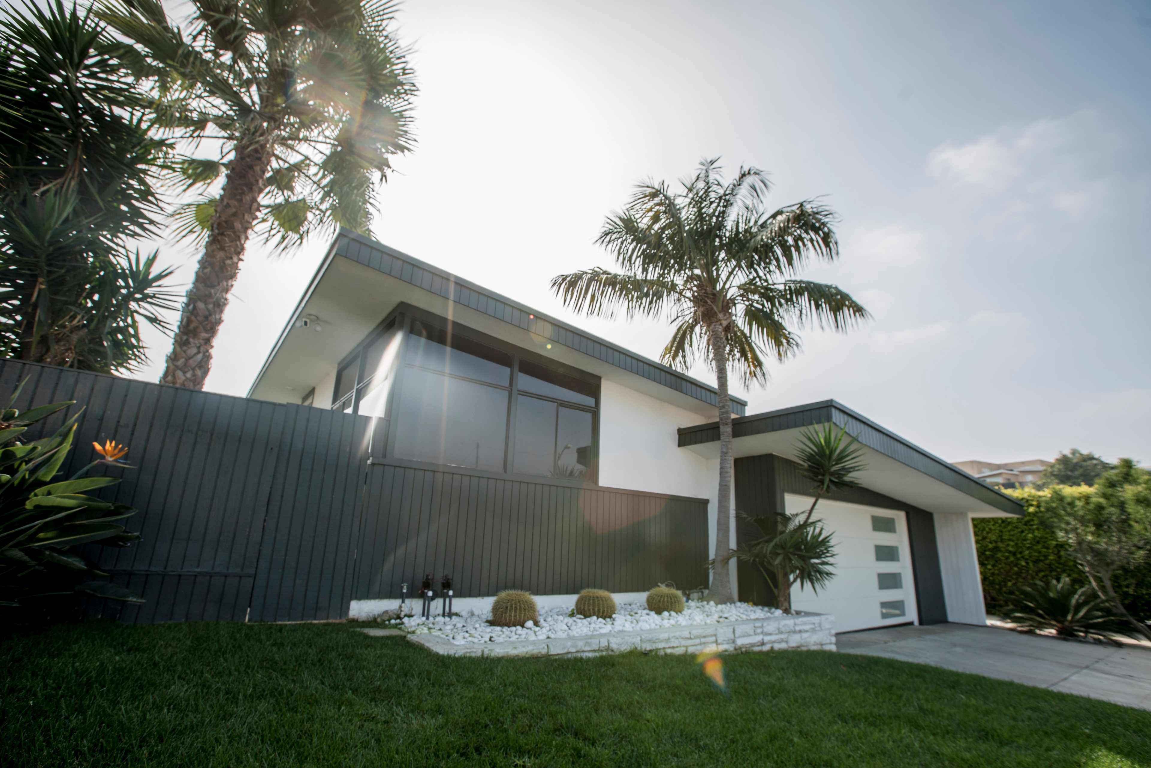 A modern house with a sloped roof is surrounded by palm trees and a neatly landscaped lawn.