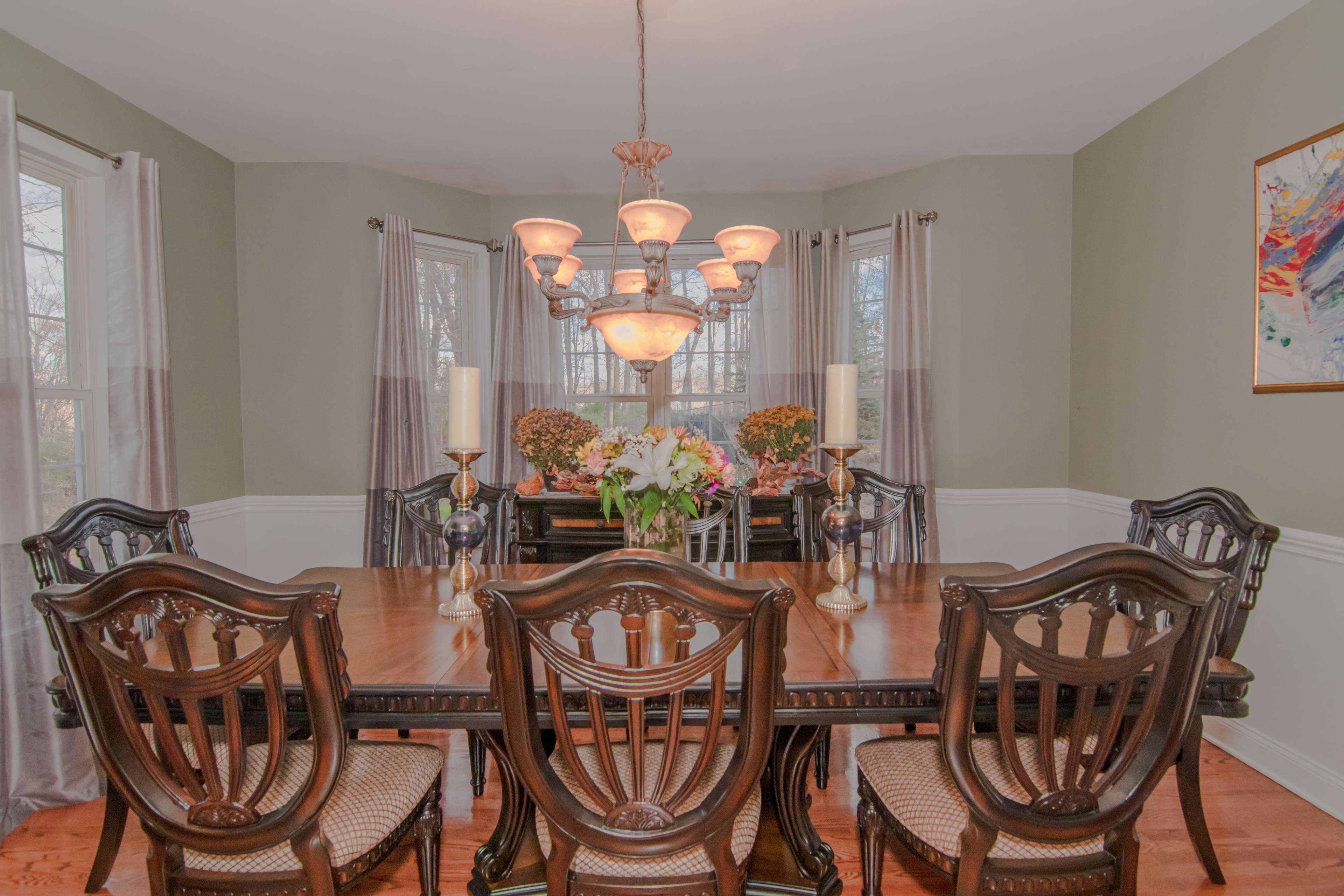 A dining room with a wooden table surrounded by six chairs, a chandelier overhead, and floral arrangements on the table.