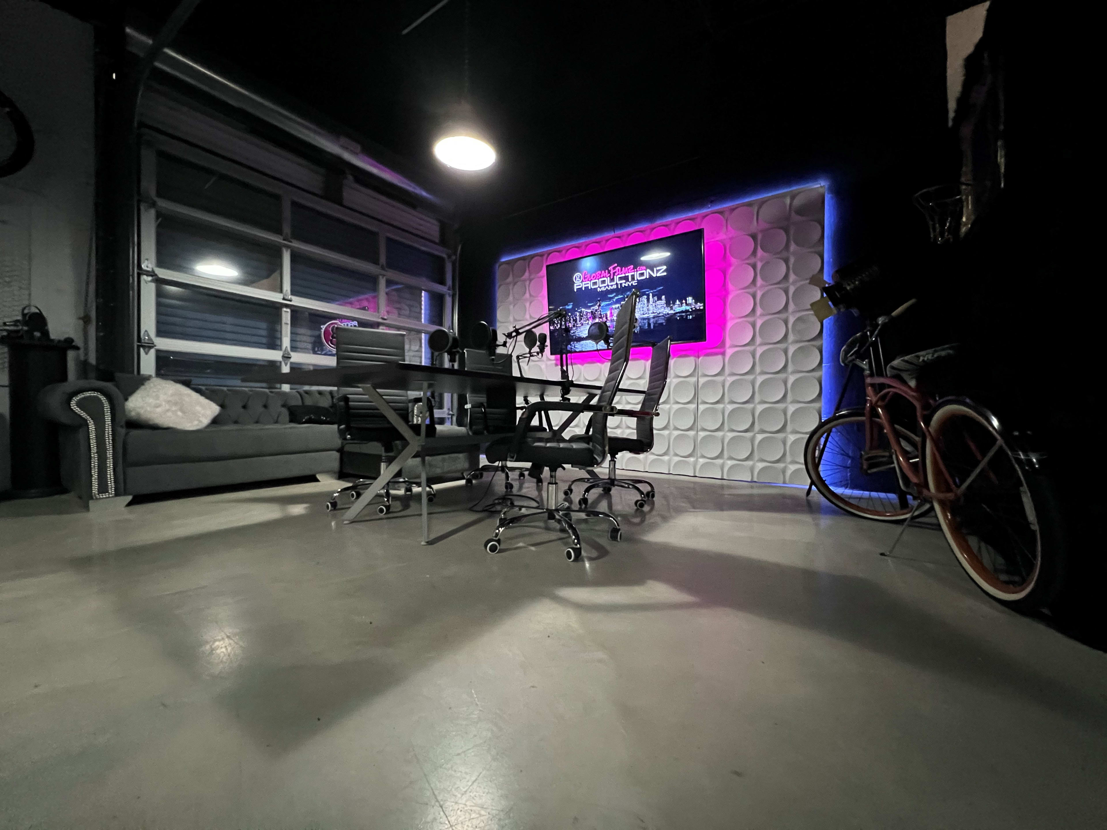 The image shows a modern office space featuring a sleek meeting table, black office chairs, and a decorative wall with neon lighting.
