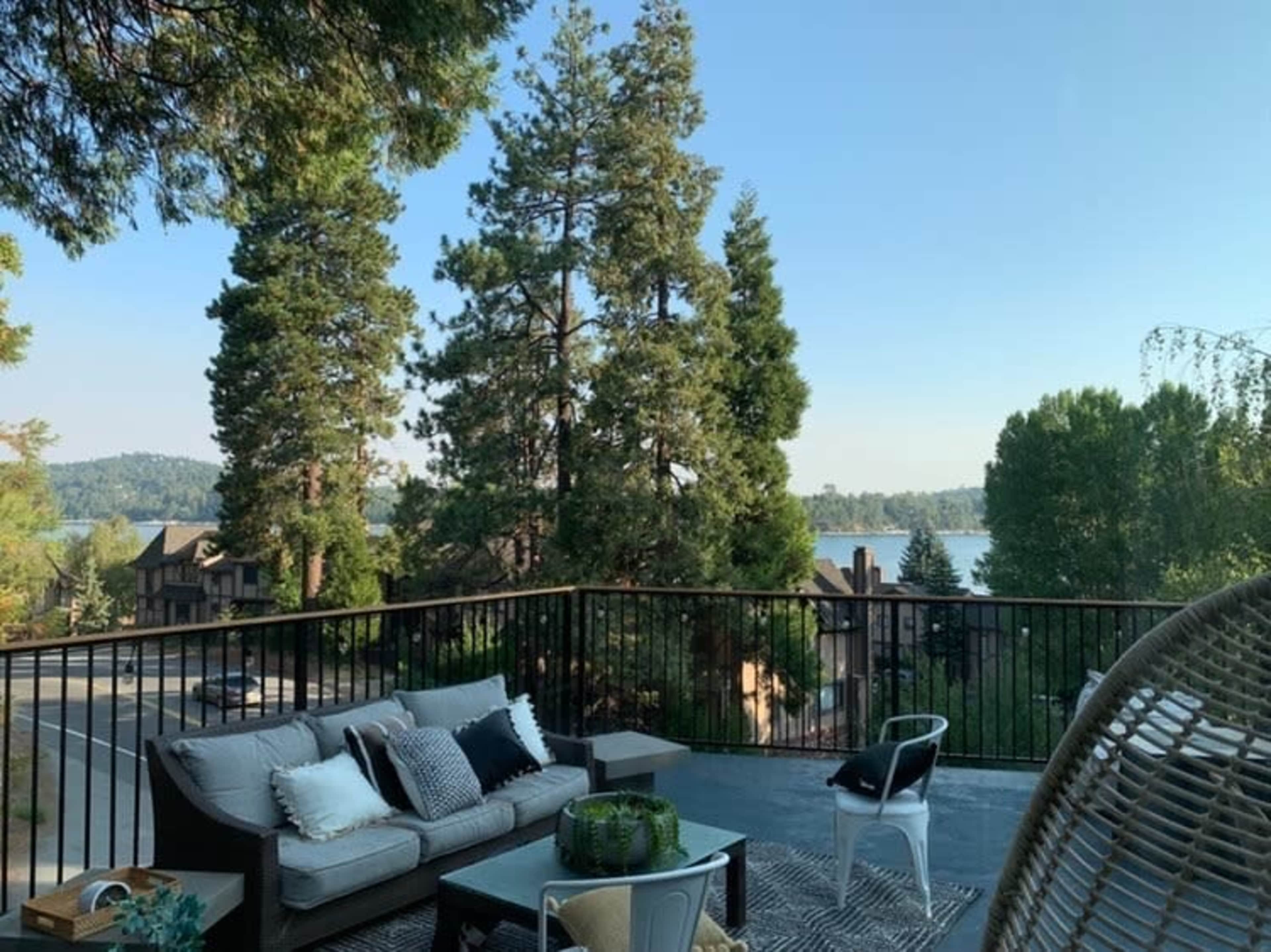 A wooden deck features outdoor furniture and overlooks a lake surrounded by trees and houses.