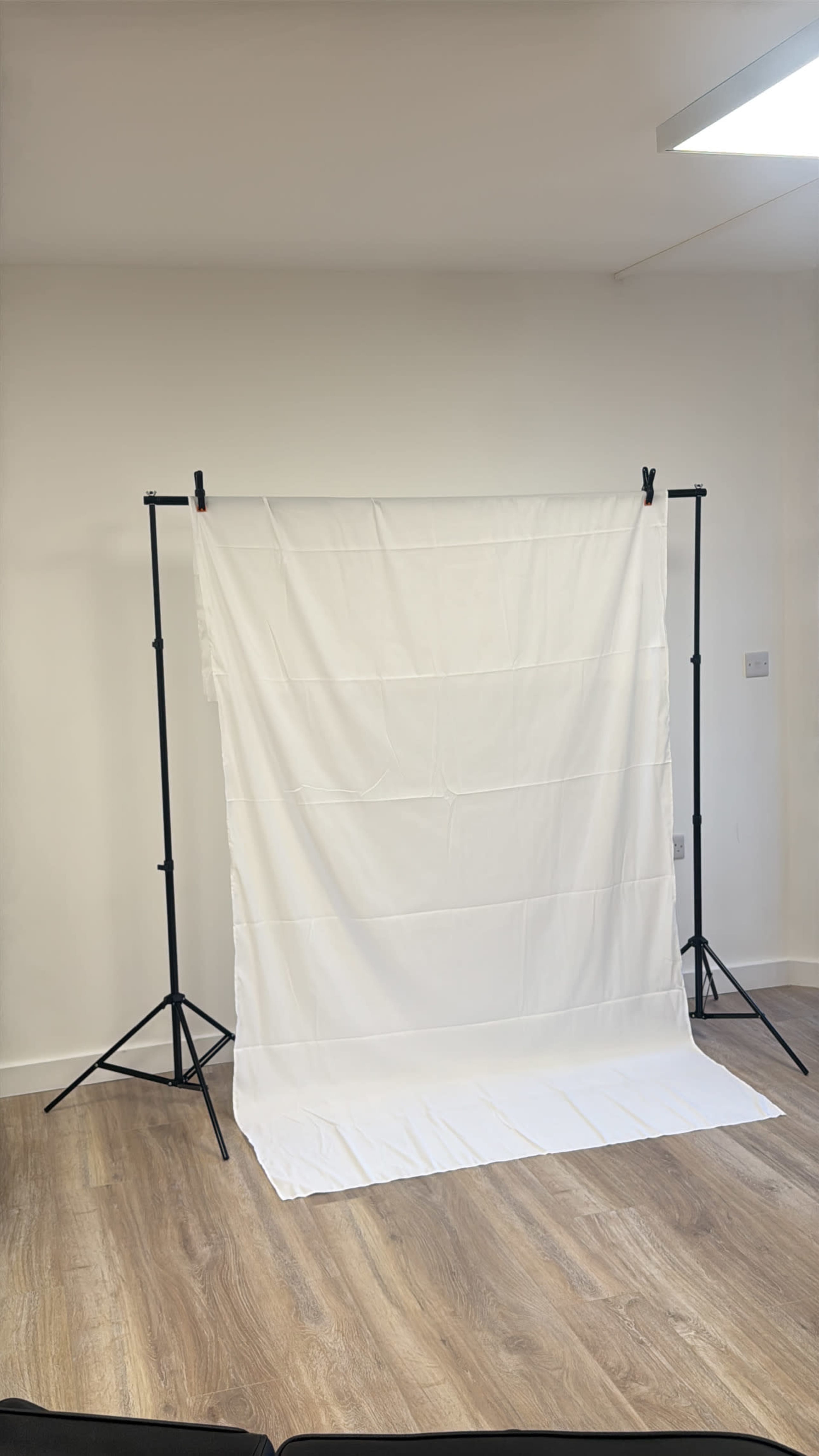 A white backdrop is set up on a black standing frame in a room with wooden flooring.