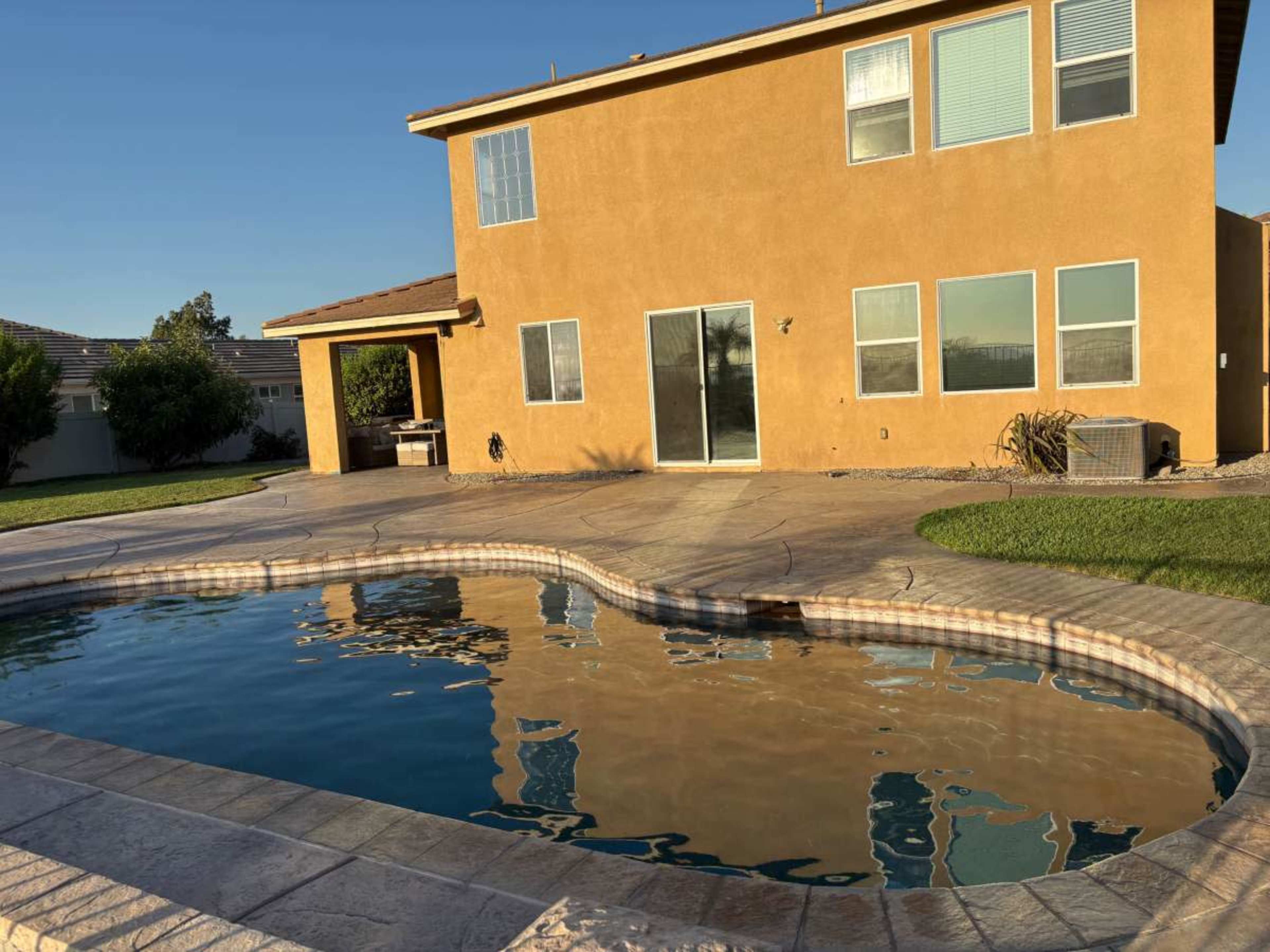 A two-story orange house with large windows overlooks a swimming pool on a landscaped lawn.